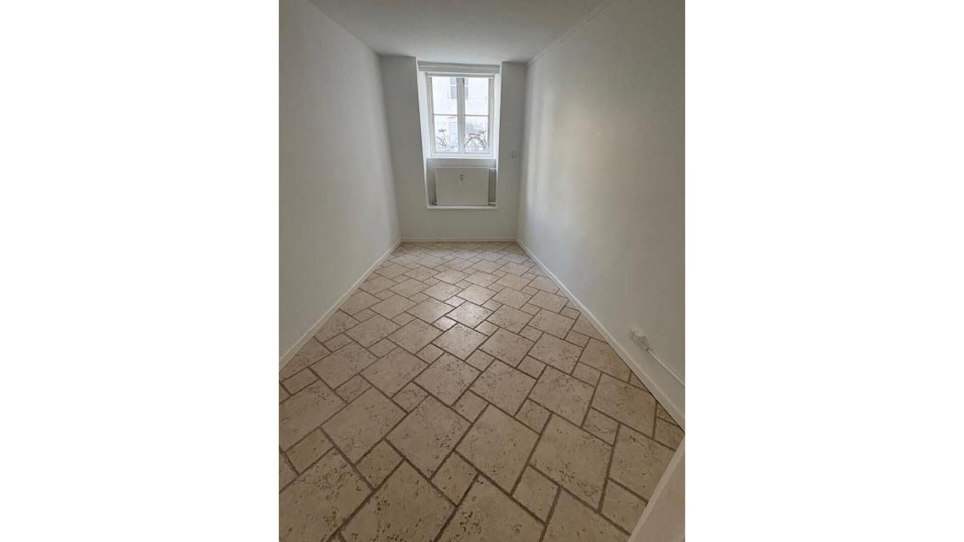 En tom og ren kontor- eller lagerlokal med hvidmalede vægge og gulvfliser med beige og brune nuancer, der er nyt og ren