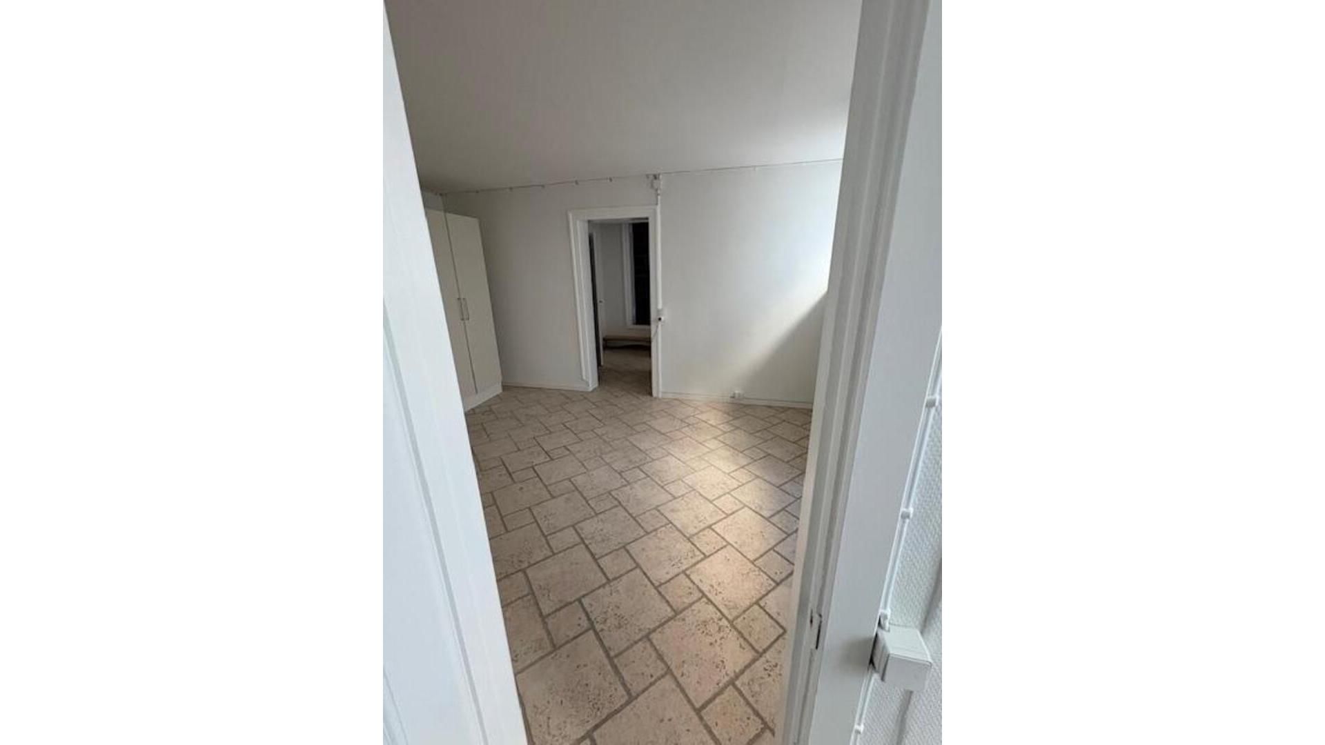 Et stort tomt rum med blanke vægge og gulv med tæppe og en dør i højre side.