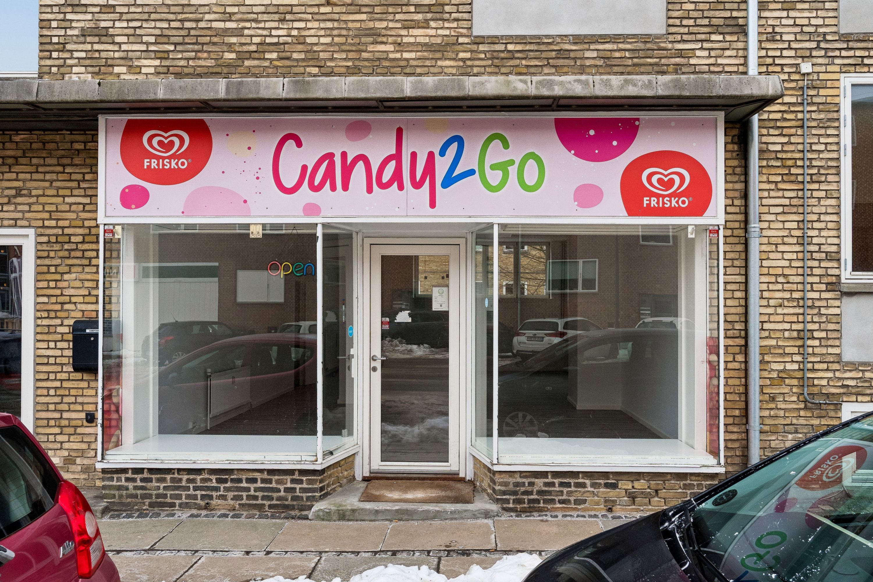 En lille butik med Candy2Go-skilt og glasdøre og vinduer i Gentofte med biler parkeret foran