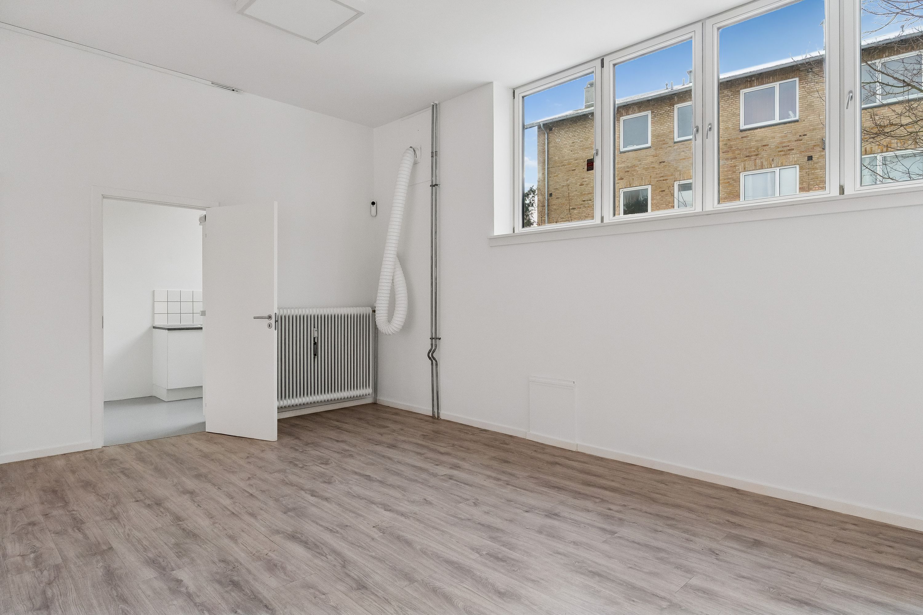 Butikslokal med pæn glasfacade og 81 m², beliggende i stueplan og åbent rum med hvide vægge, gulv og radiator samt vinduer med udsigt til bygningen udenfor