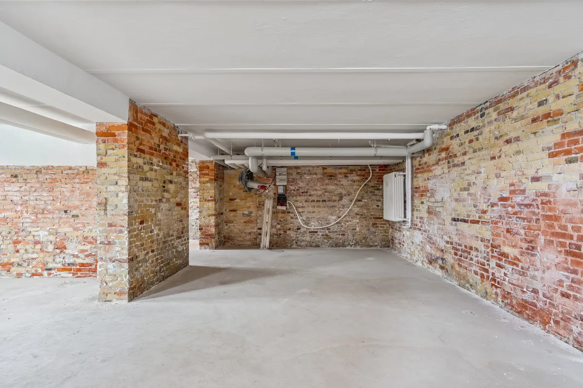 Lager til leje med røde mursten og hvidt loft. Rør i loftet og et skur på væggen. Væggen er fuld af røde og gule mursten.