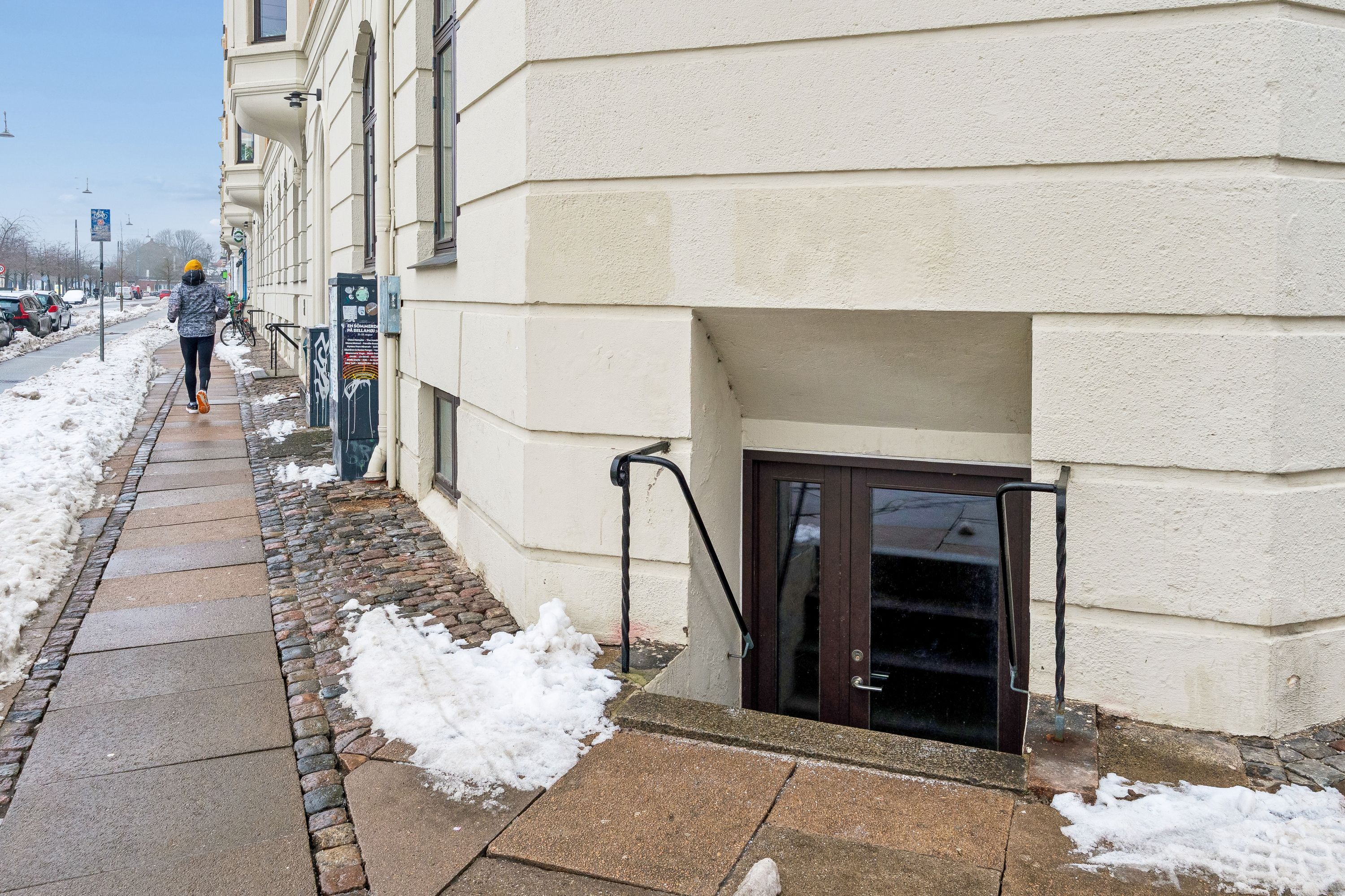 Kvinde går på fortov med snebrædt og skovl i hånden uden for Islands Brygge 19, hvor lagerlejligheden er til leje i København