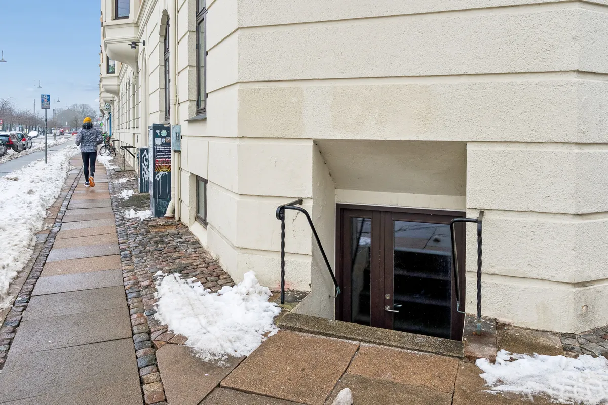 Kvinde går på fortov med snebrædt og skovl i hånden uden for Islands Brygge 19, hvor lagerlejligheden er til leje i København