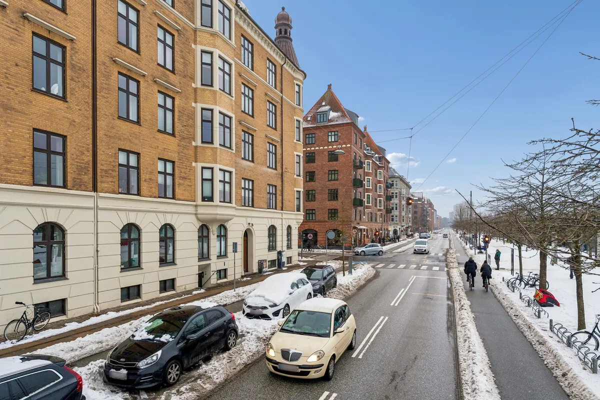 Køretøjer kører på Islands Brygge i København med sne dækket vej og mennesker går på cykelstier og fodgængerovergang