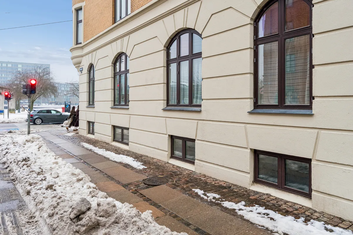 Et hjørnehus med beige væg og vinduer med brune rammer og skur er det første, man ser på Islands Brygge 19 i København S