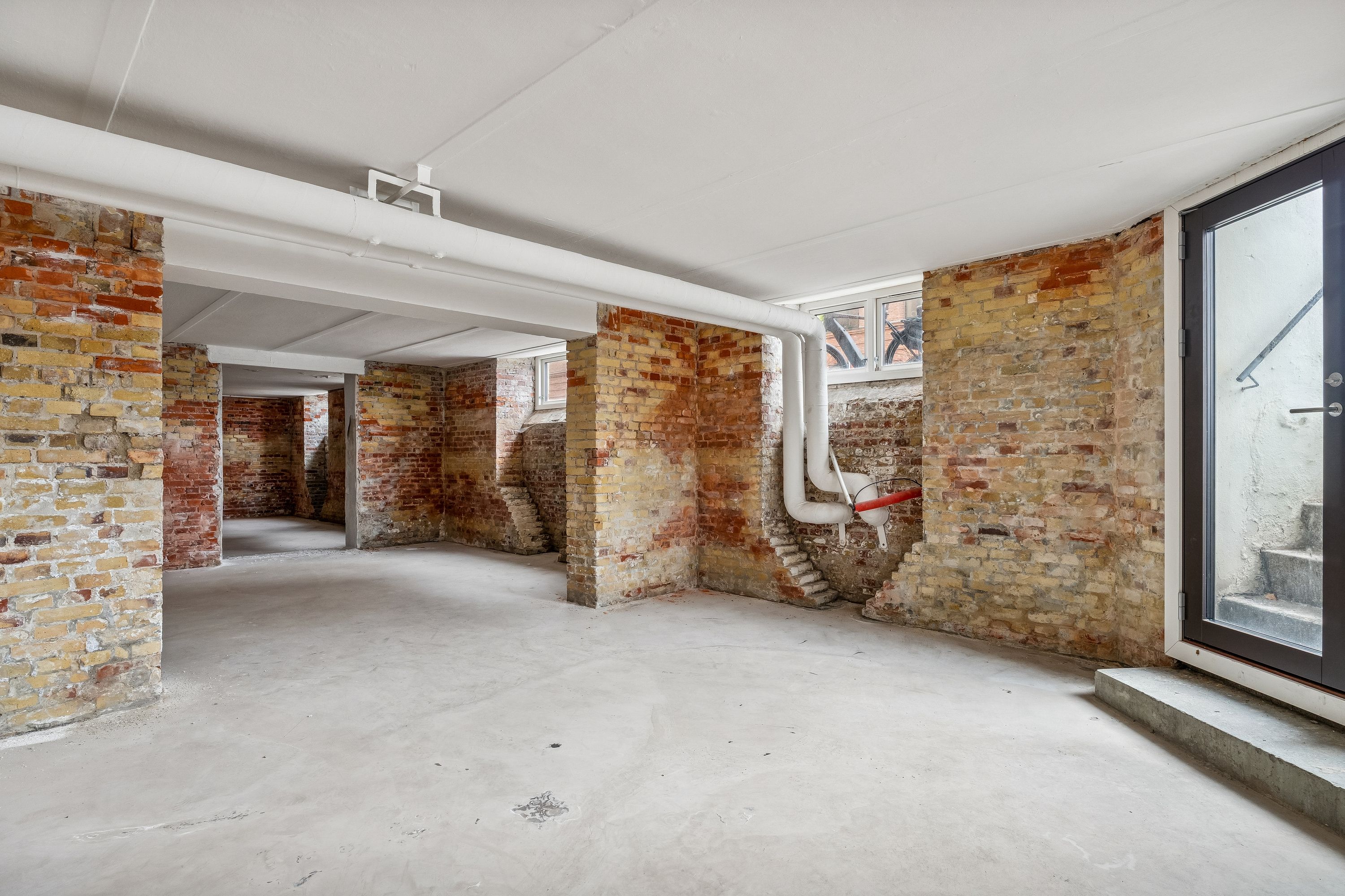 Lagerrum med røde mursten og lyse lofter. En stor rødt murstensvæg med lyse lofter og røde murstenssøjler. Et hjørne med lyse lofter og rødt murstensmønster