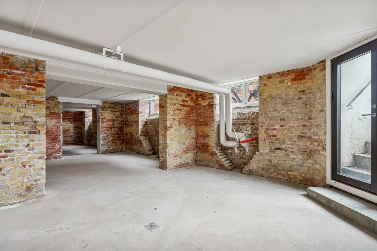 Lagerrum med røde mursten og lyse lofter. En stor rødt murstensvæg med lyse lofter og røde murstenssøjler. Et hjørne med lyse lofter og rødt murstensmønster