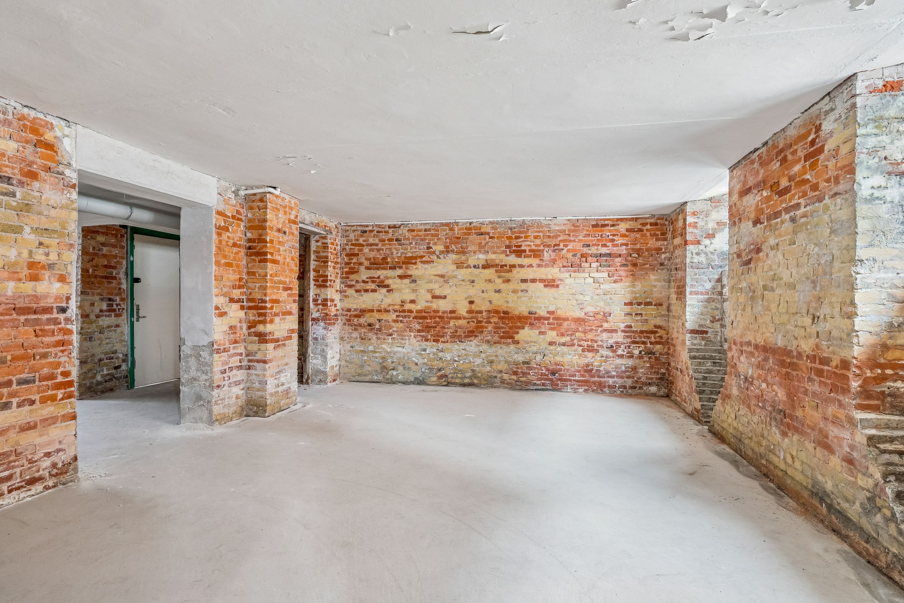 Lagerrum med højt hvide loft og røde murstensvægge i lejligheden på Islands Brygge 19 i København S. Lejligheden har to gange og to kolonner med cement.