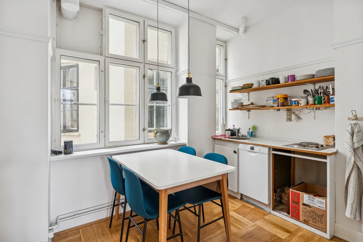 Lys og rummelig lejlighed med terrasse og udsigt, moderne køkken med lyse krydderurter og lysekroner, blå stole ved spisebordet, åbent vindue og udsigt til Ørstedsparken, Nørreport Station og Rådhuspladsen