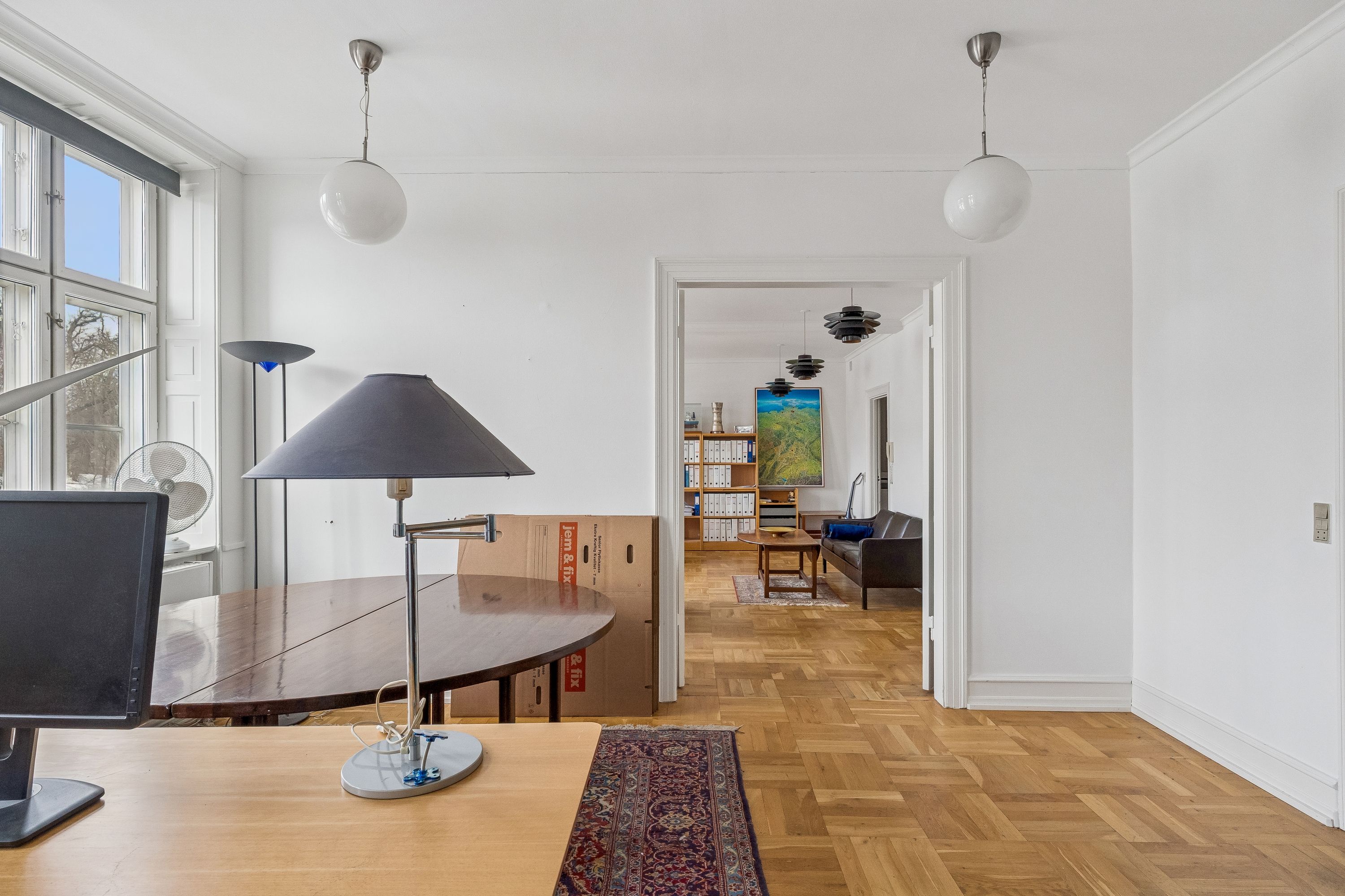 Lejlighed med lys og rummelig stue, møbler og lysekroner, trægulv og vinduer med udsigt til haven