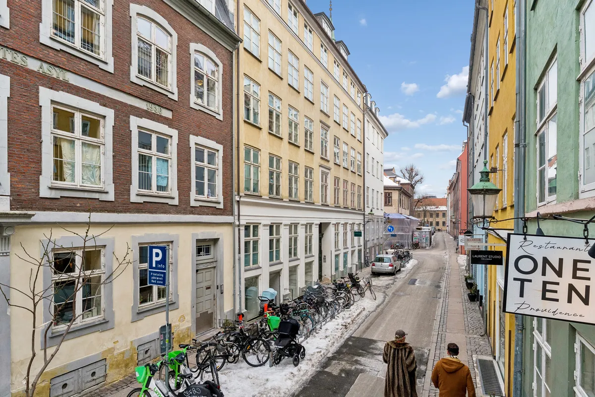 Gadebillede med parkerede cykler, to mennesker og en restaurantskilt med teksten "ONE TEN Providence" i København, med sne på jorden og farverige bygninger