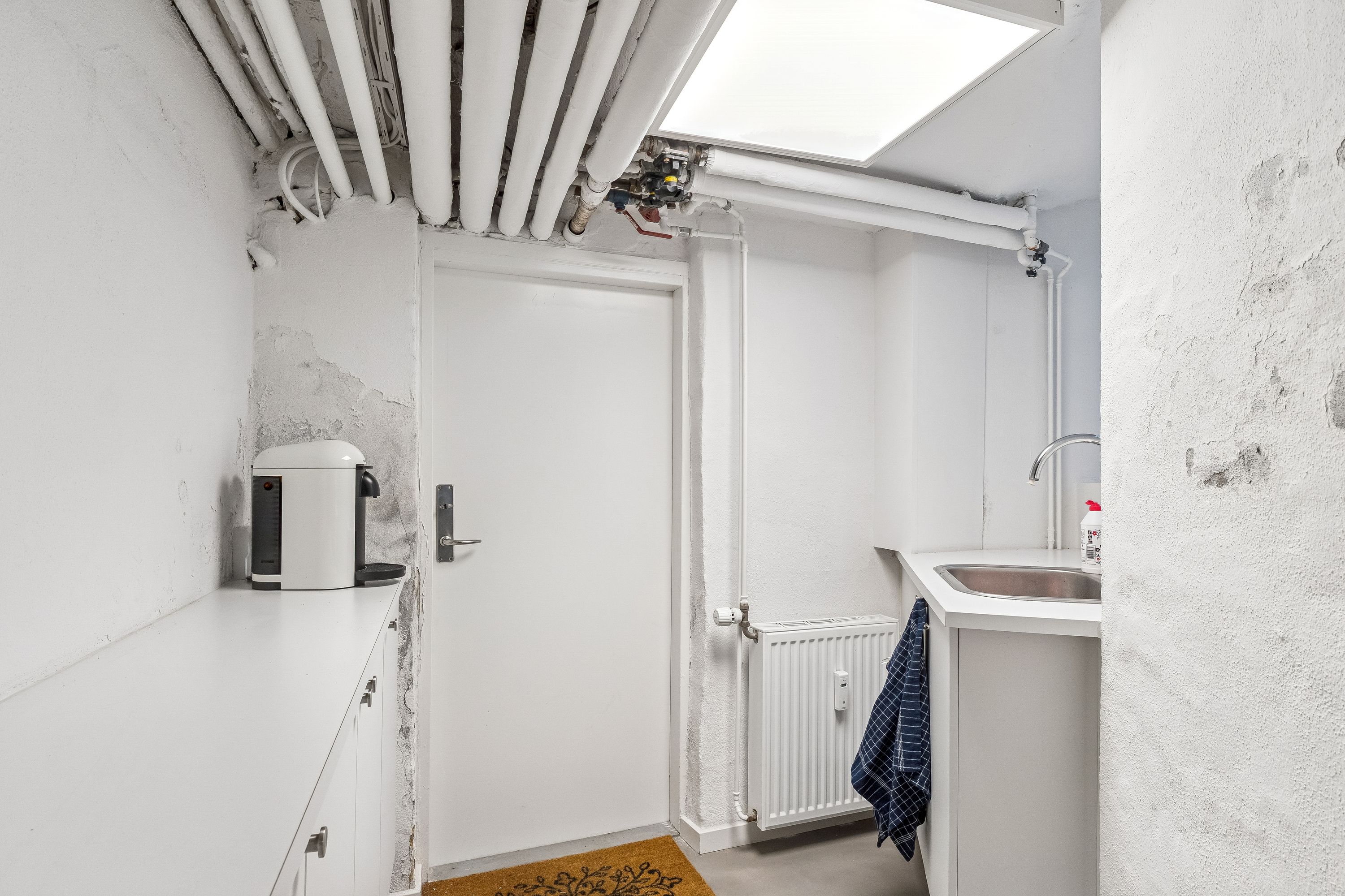 Lyst og rent rum med moderne design, hvidt køkken med vandhaner og radiator, ren gulv og hvide vægge. Enhver kan nyde den velplejede og pæne atmosfære.