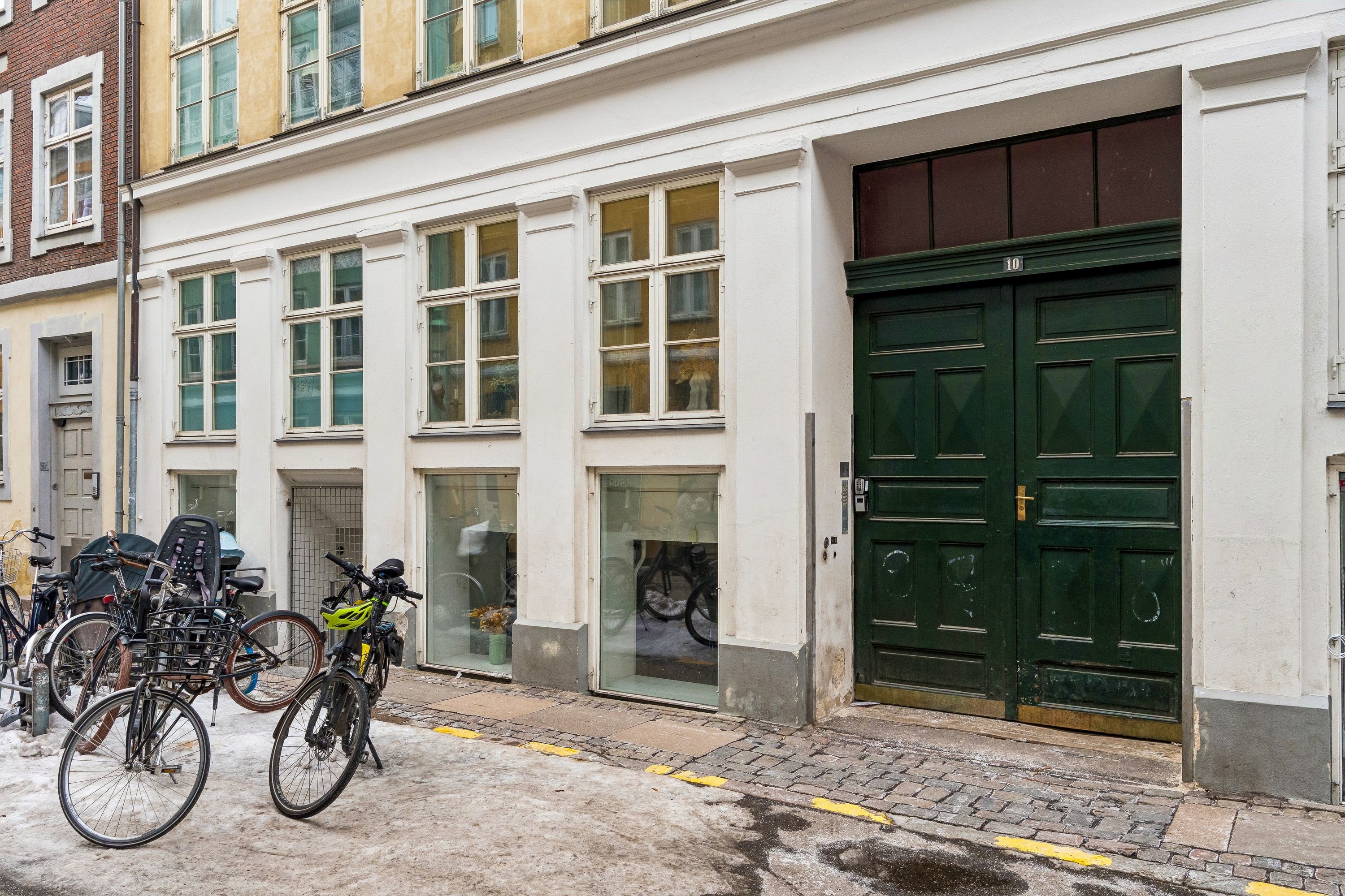 Kontor til leje på Sankt Peders Stræde 10 i København K. Bygningen har moderne betonlook-gulve, hvide vægge og lofter, og en stor grøn dør. Adgangsvejen er stenbelægget.