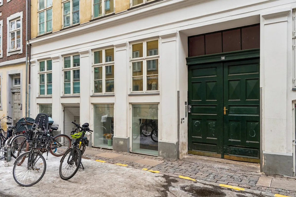 Kontor til leje på Sankt Peders Stræde 10 i København K. Bygningen har moderne betonlook-gulve, hvide vægge og lofter, og en stor grøn dør. Adgangsvejen er stenbelægget.
