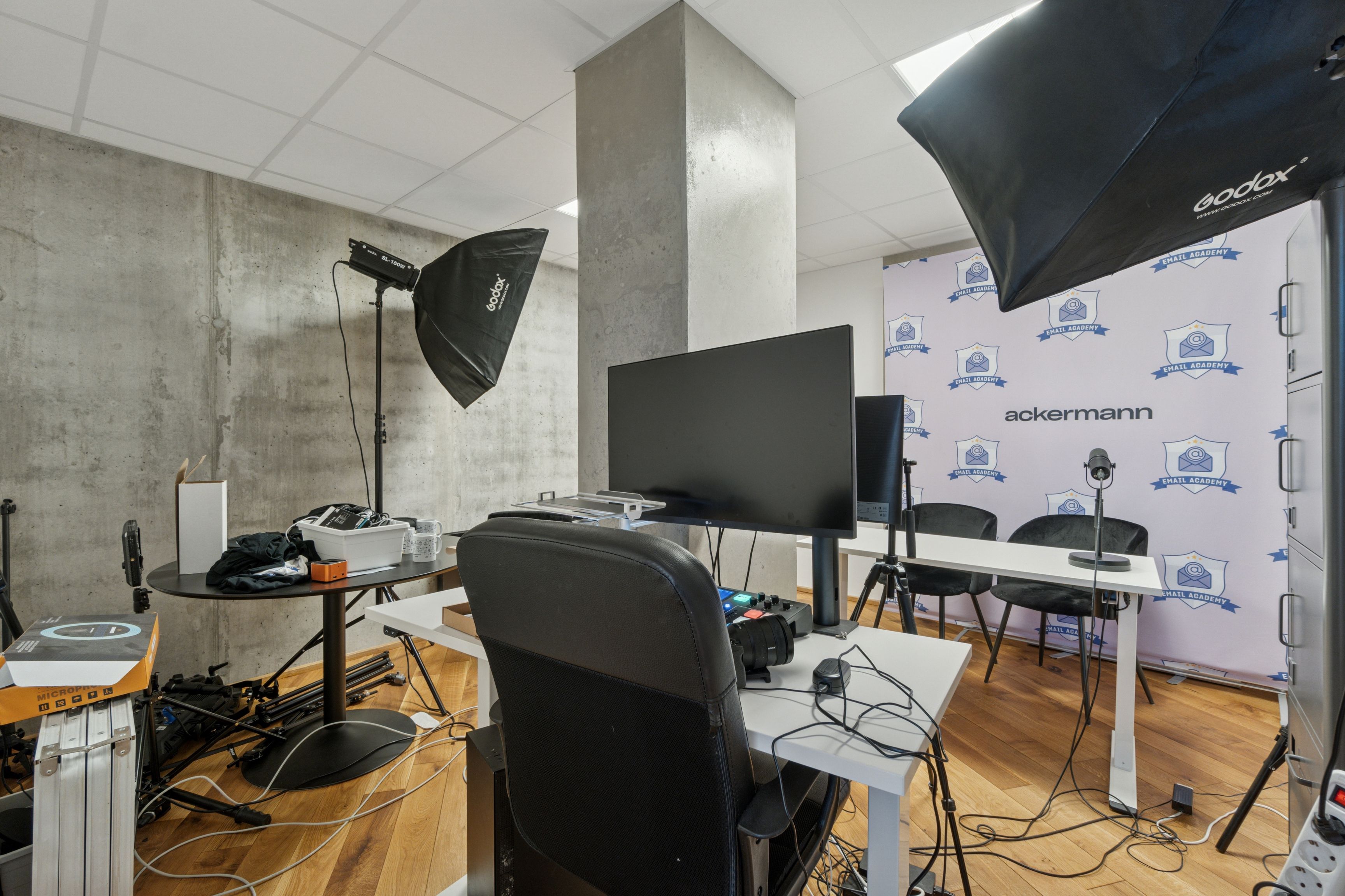 Moderne kontor med to store skærme, stol og bord samt to stålampe med paraply. Dekoreret væg med flere loger og mærker.