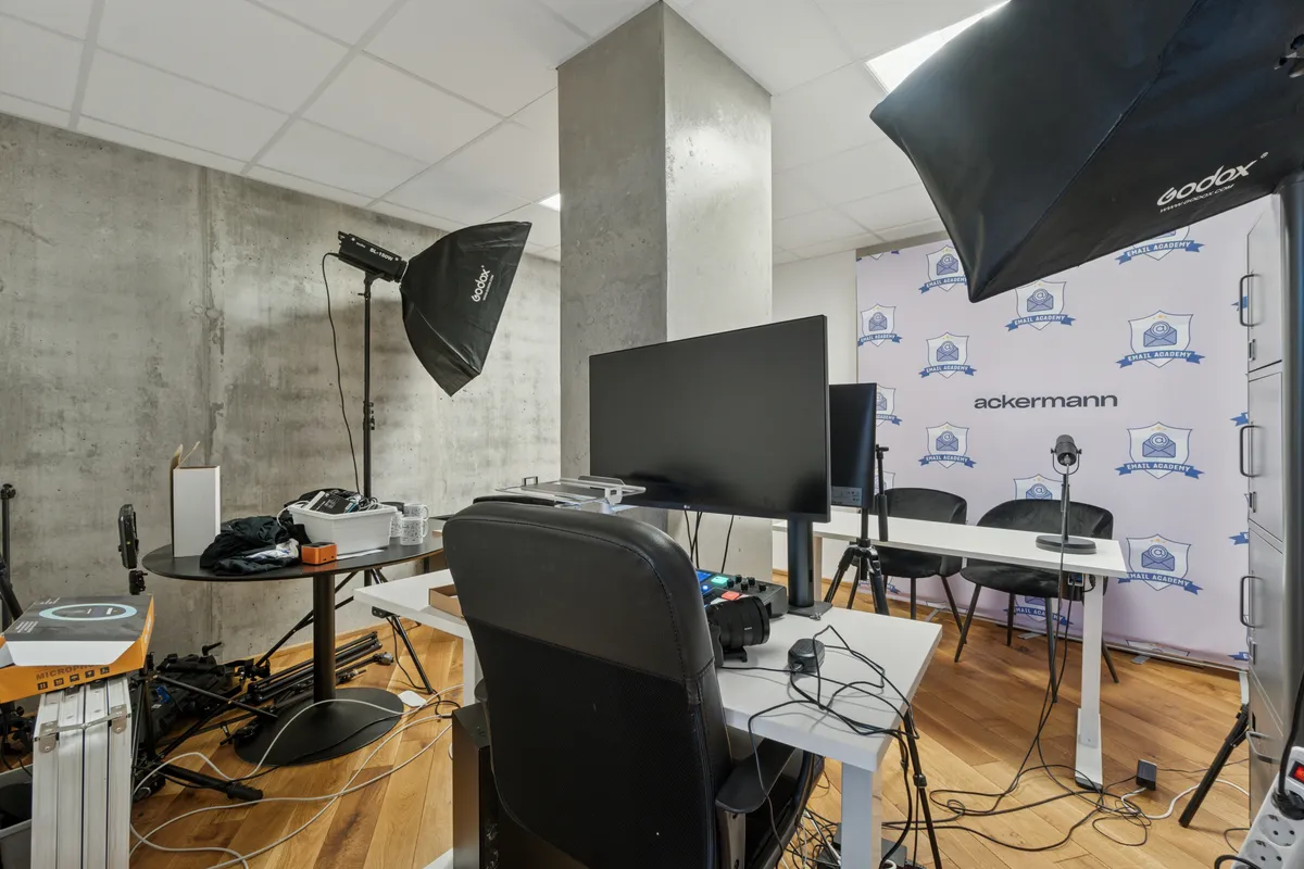 Moderne kontor med to store skærme, stol og bord samt to stålampe med paraply. Dekoreret væg med flere loger og mærker.