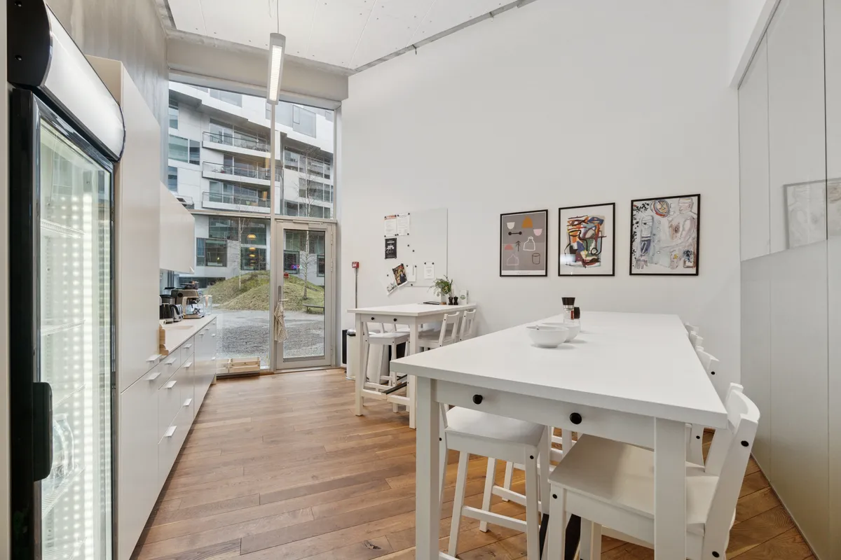 En moderne kontor med lyse vægge, et hvidt bord, og lyse stolene og lysekroner samt en køleskab og en udgang til gården