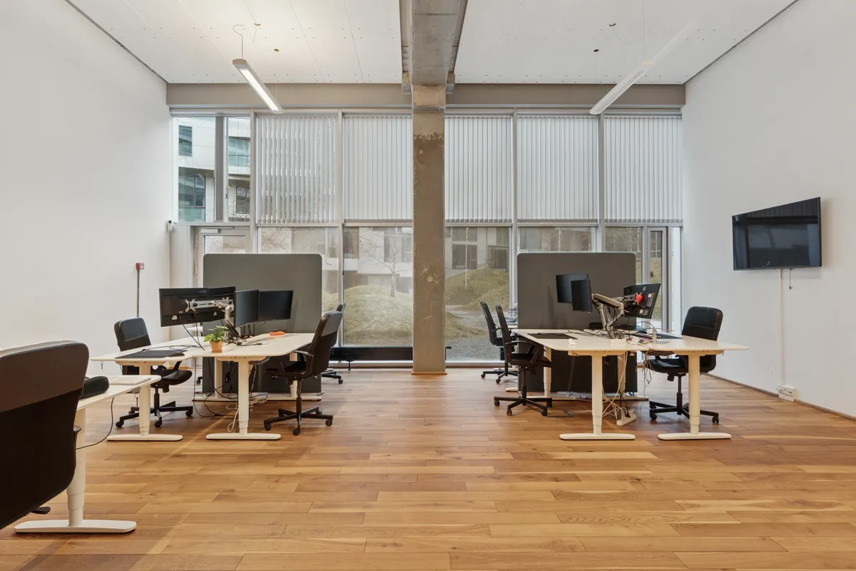Et moderne og rummeligt kontorlejemål med lyse gulve, hvide vægge og store vinduer, der giver masser af naturlys og udsigt til byen