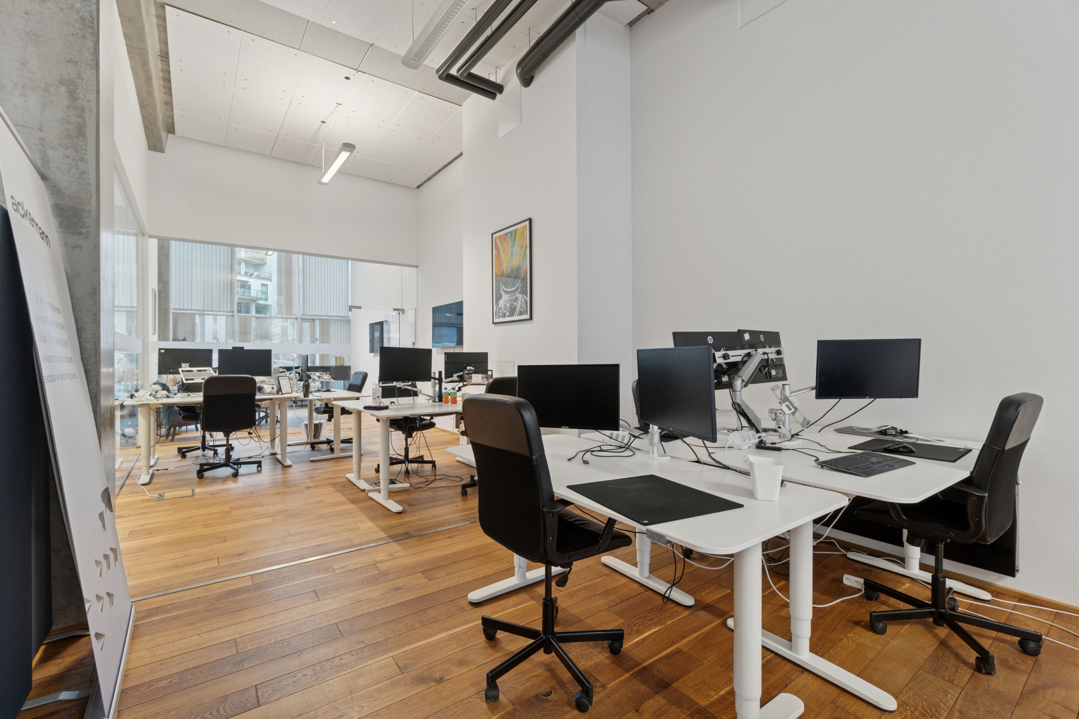 Kontorlejemål med moderne skriveborde og stole, computere og flere glasvinduer med byudsigt