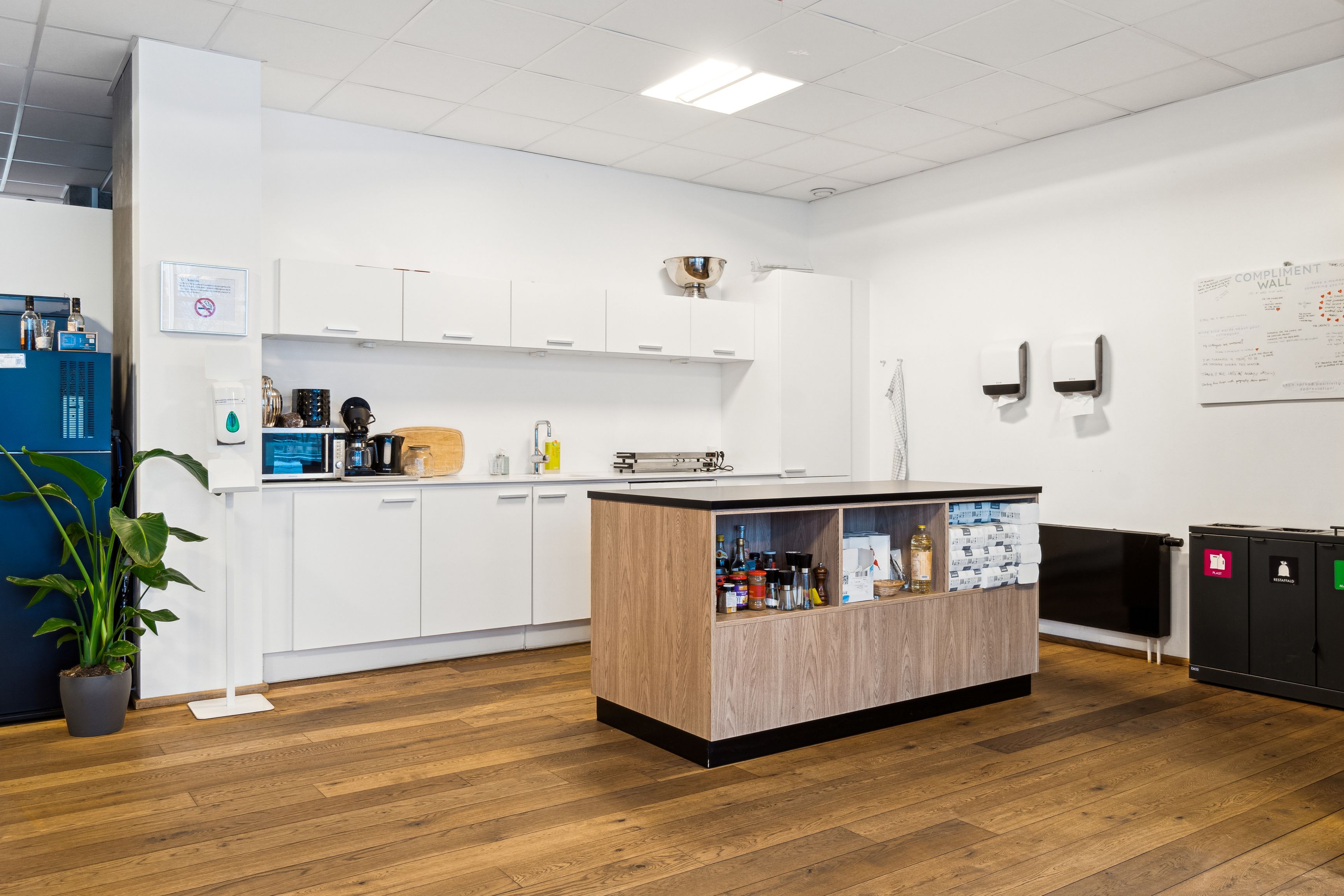 Kontor med højloft og lyse vægge med komplet køkken og tekøkken. Komplet indretning med moderne apparater, og et smukt designet tekøkken med åbent skab og lyse møbler.