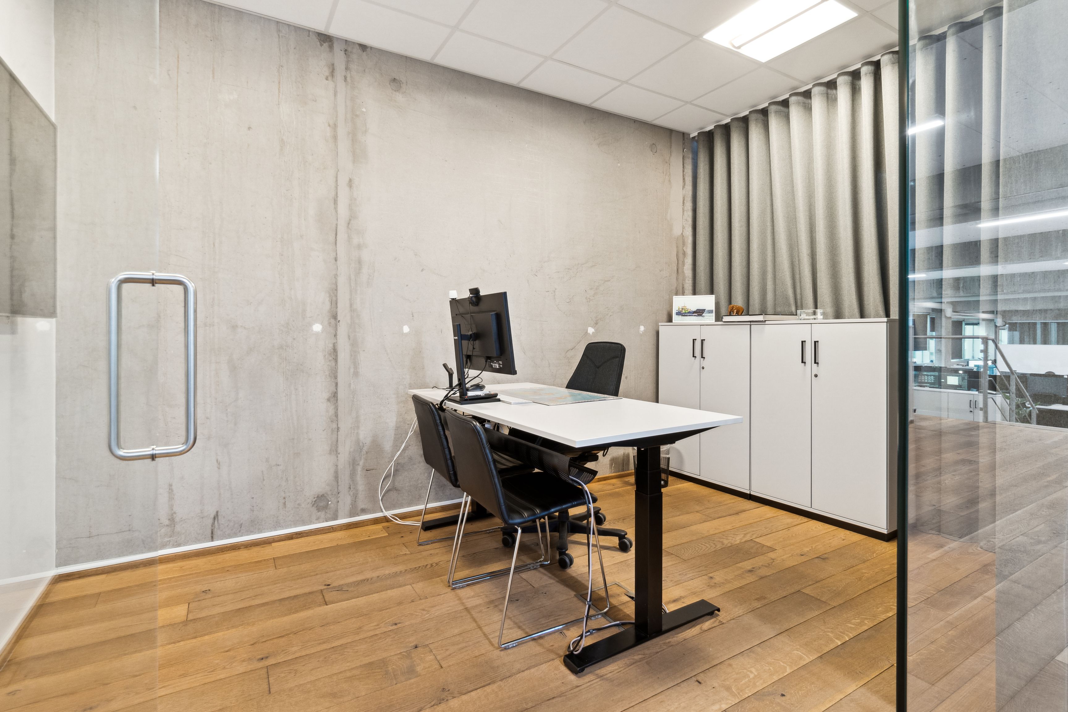 Kontorrum med høj glasdør, moderne bord, computer og stol samt hvidt skab og lysegardiner i københavnsk erhvervslejemål