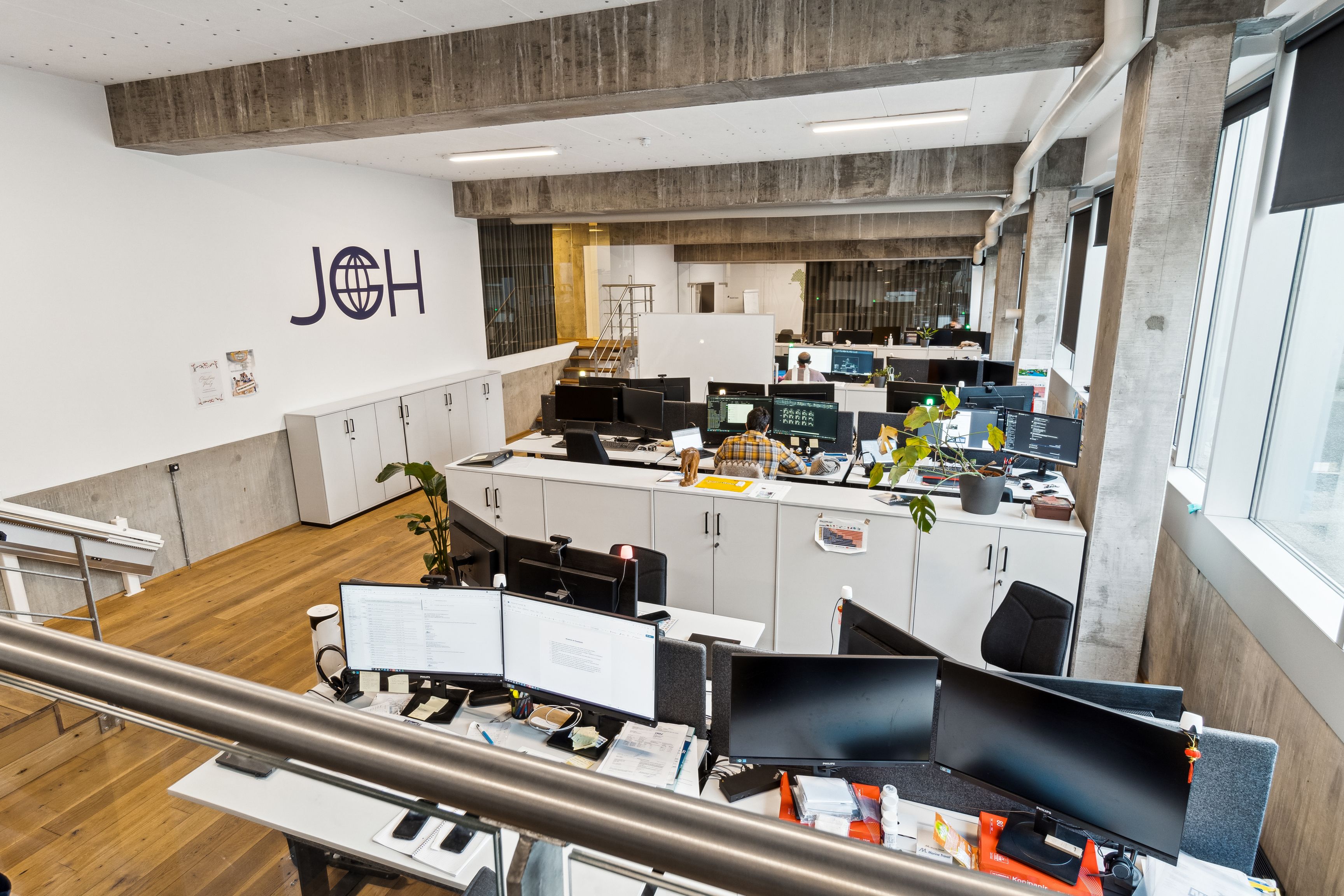 Kontorrum med moderne design og lyse vinduer, møbler og teknologi fordelt med fokus på arbejdsområder, hvor folk arbejder på computere.