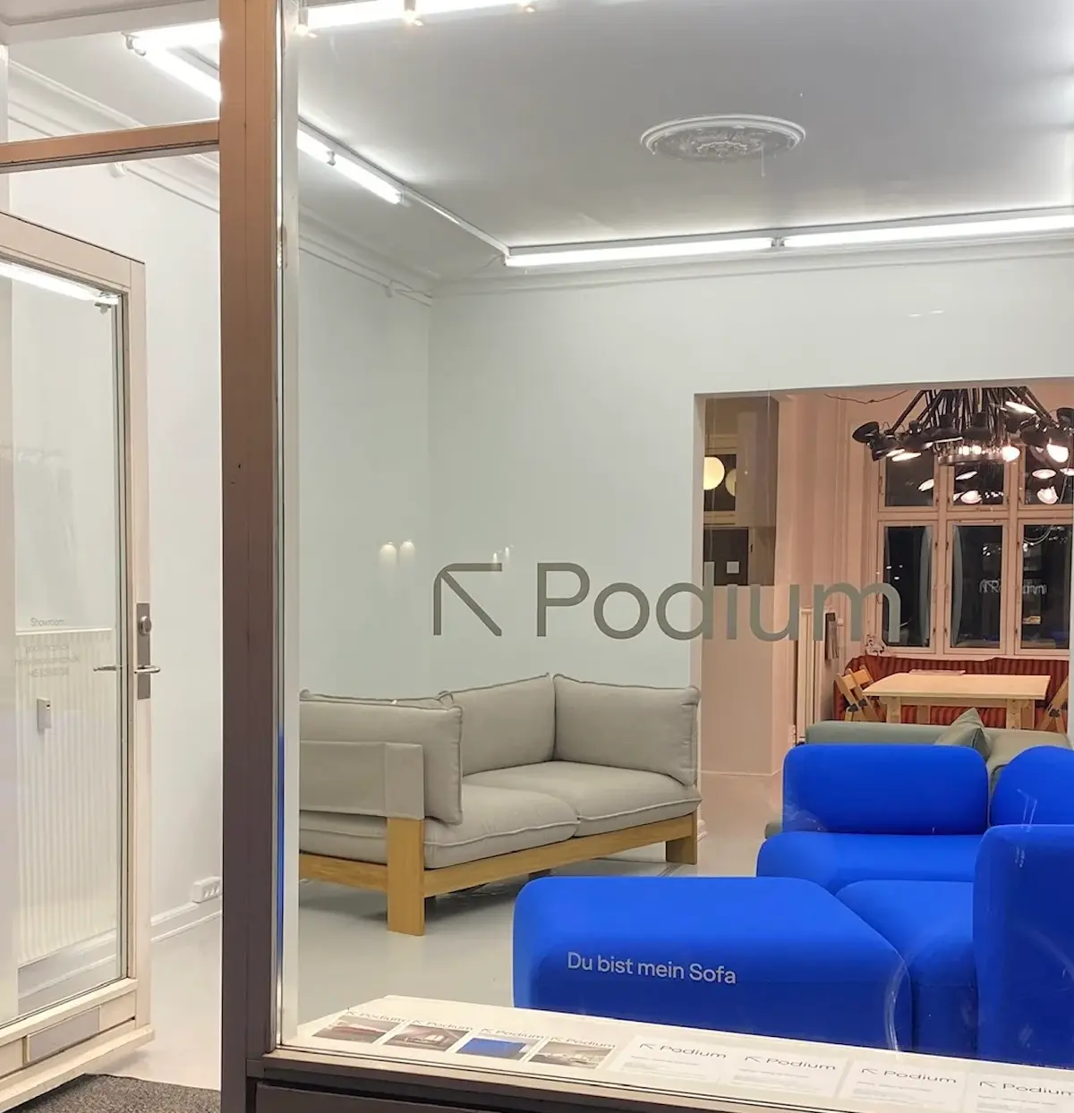 Butik med Podium møbler og sofaer i lyse farver med Podium-logoet på vinduet. Lys og moderne møbler i lyse farver med træelementer.