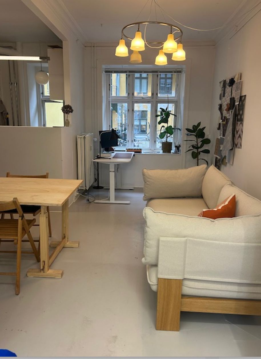 En simpel indretning med hvidt loft, hvide vægge, en hvid sofa med pudsede hvidt sæde og røde puder, og et bord med stole