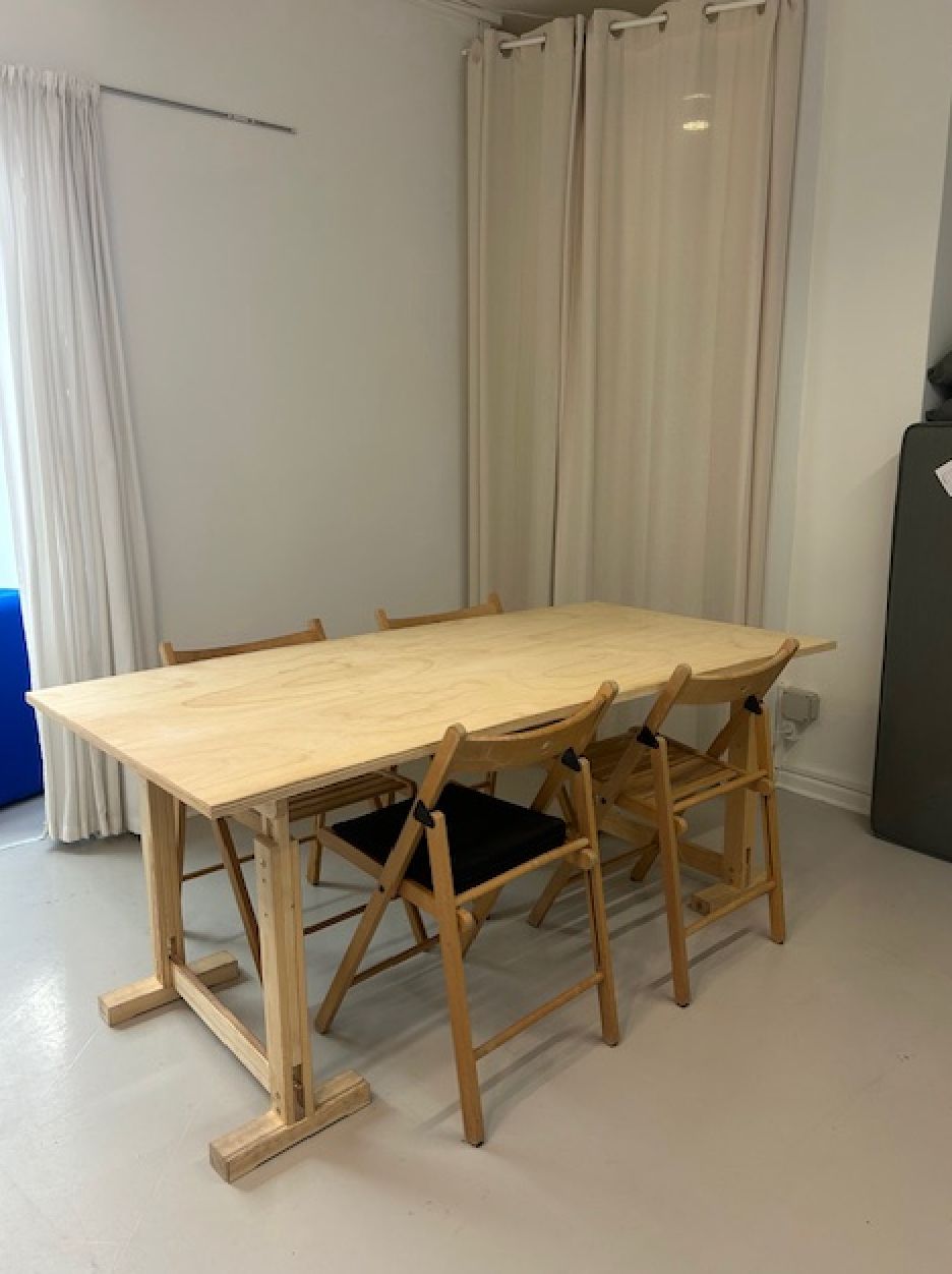 Langt, træbord med fire stole i en stor, rummelig stue med hvide vægge og gardiner samt en blå sofa.