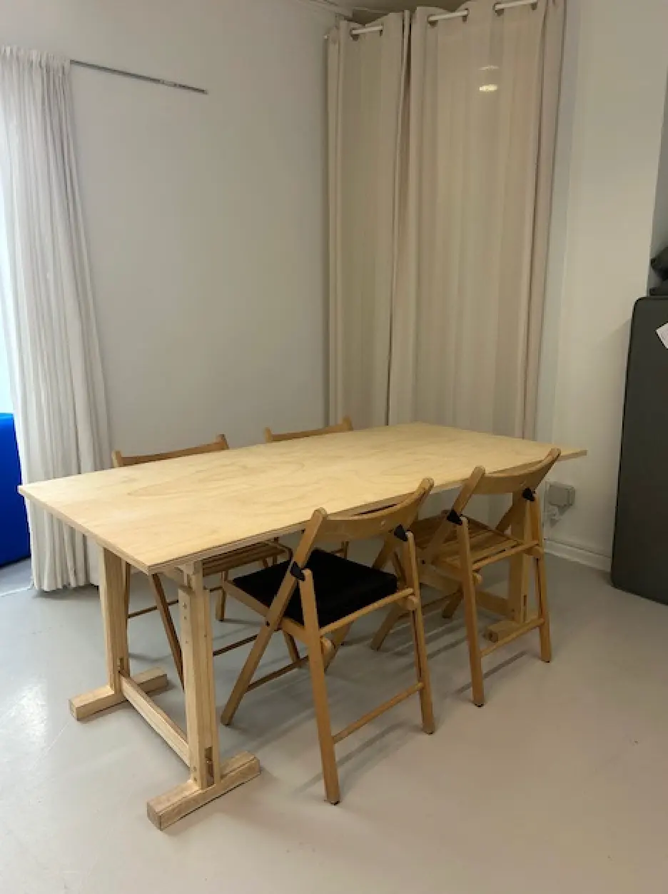 Langt, træbord med fire stole i en stor, rummelig stue med hvide vægge og gardiner samt en blå sofa.