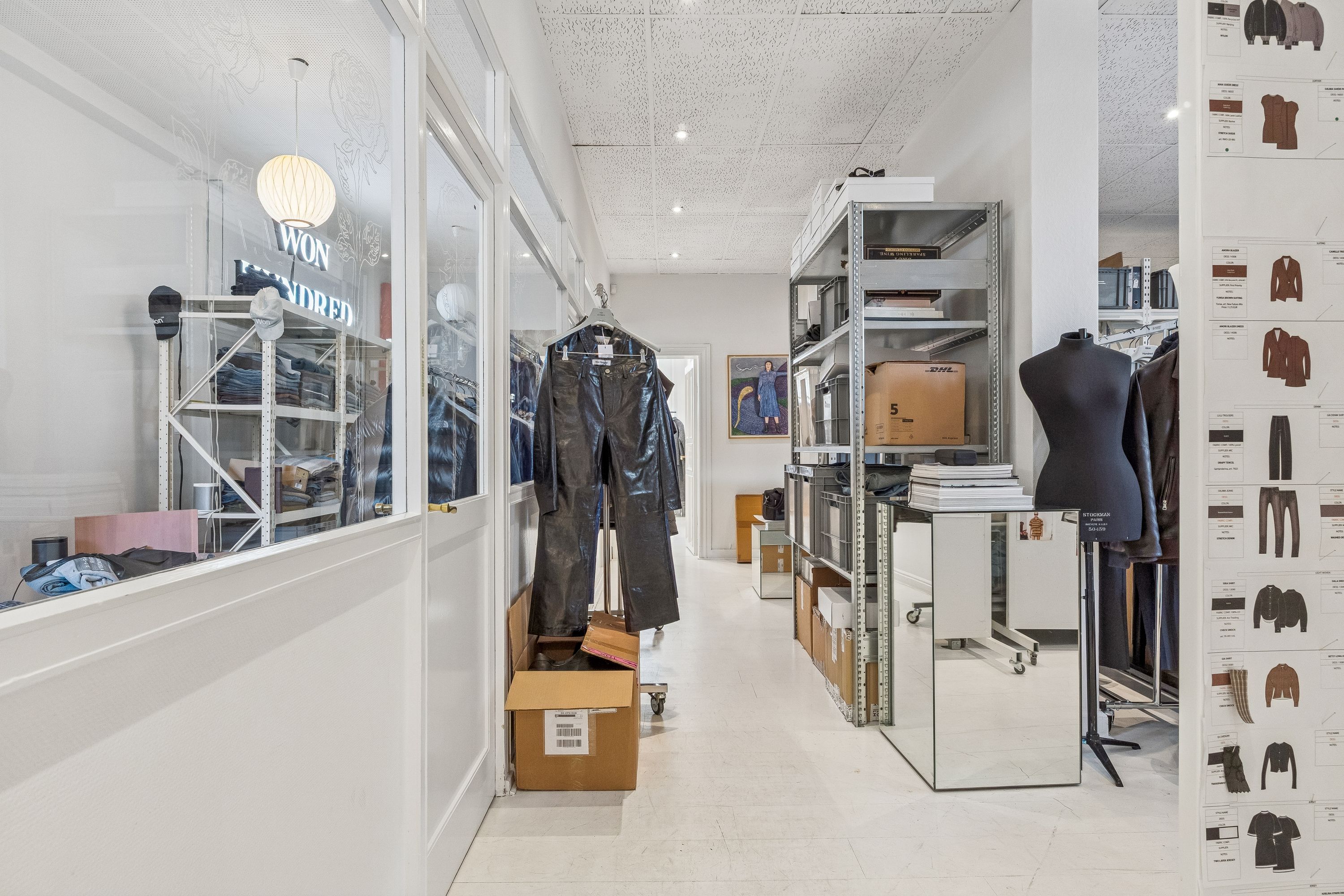 Kontor i Frederiksberg med lyse vinduer, moderne møbler, tøjstative, bokse, og en lys gulvbelægning. Farverige tøjstykker og et billede på væggen.