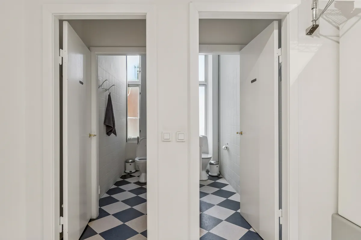 Åbne hvide døre med tæppe og to toiletter i hver side og lysegule vægge med enhver detalje.