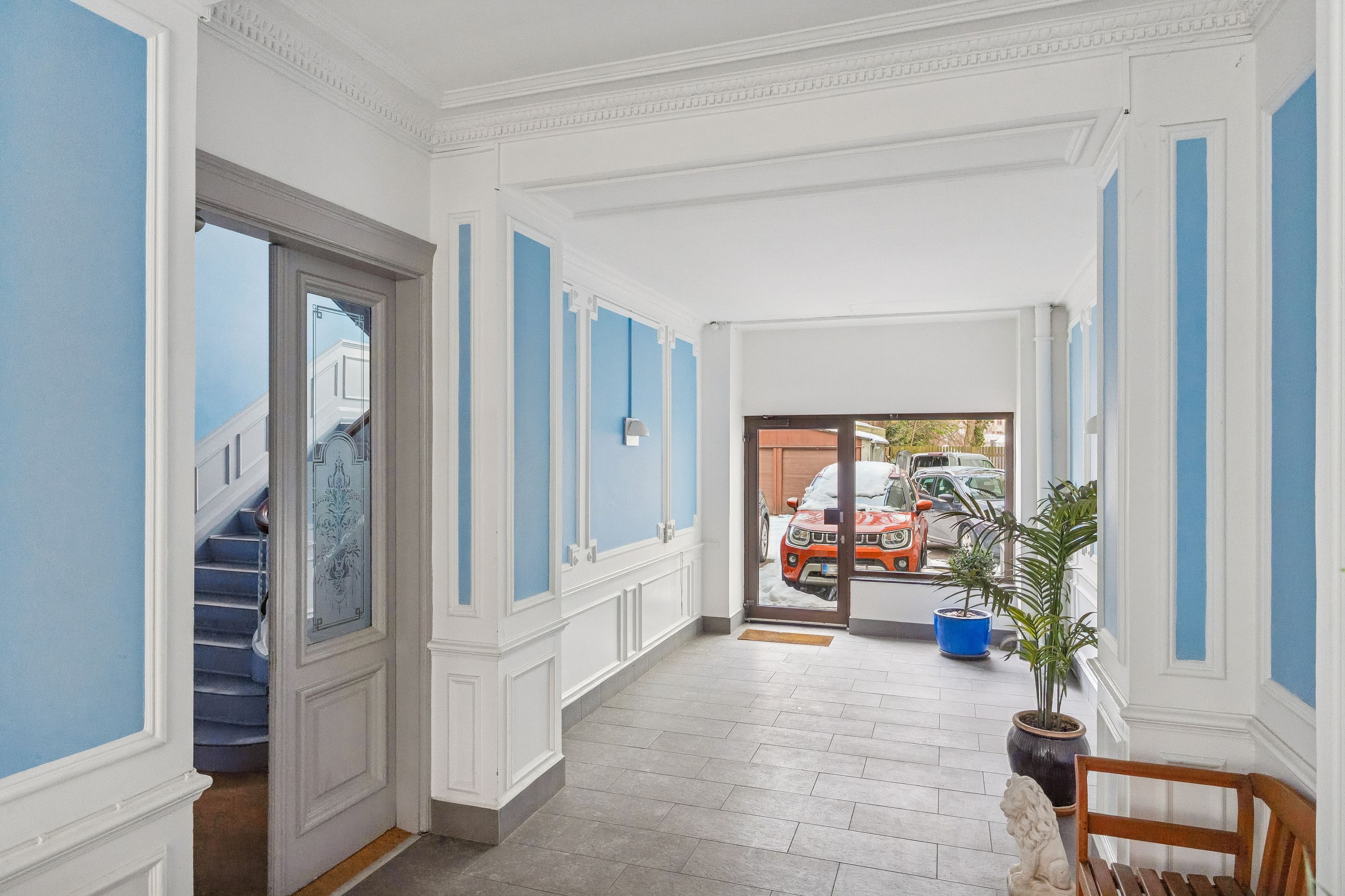 Kontor til leje på Gammel Kongevej 102 i Frederiksberg med en stor forhal og to døre. En lyseblå og hvid væg og en træstol med en lille statue.