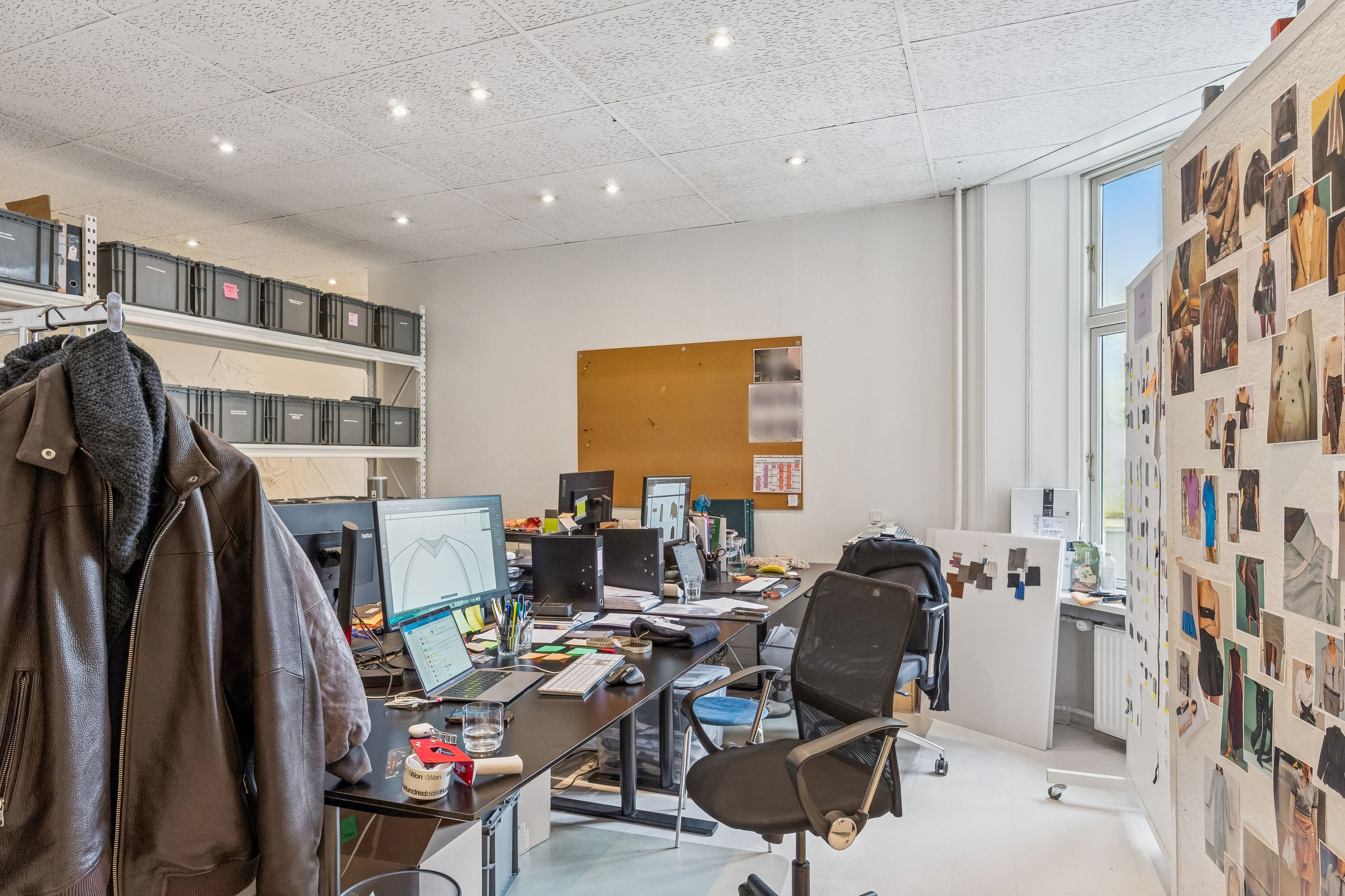 Kontorrum med møbler, monitorer, klædeskab, hængsel og billeder på væggen