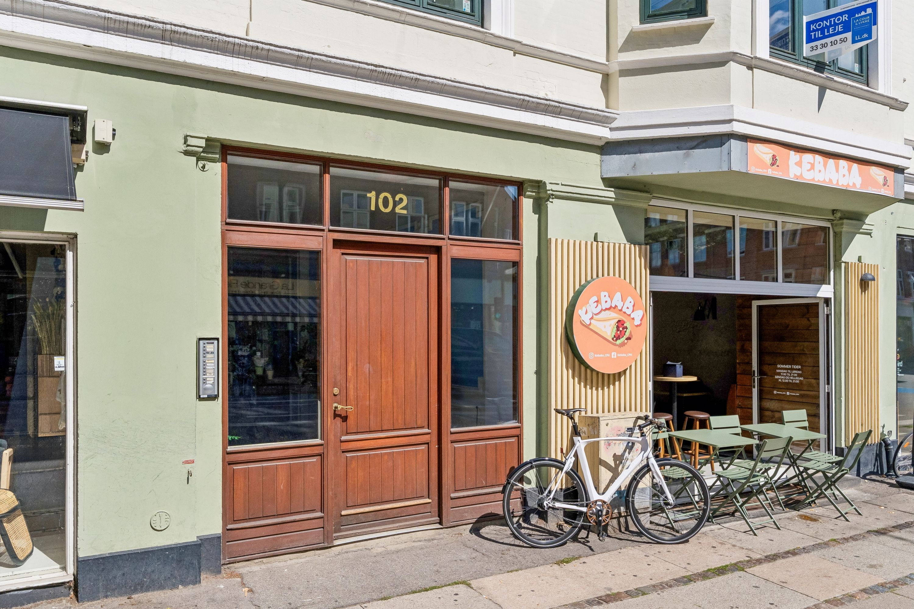 Kontor til leje på Gammel Kongevej 102. Bygningen har glasdøre, grønne vægge og en stor søjle. Der er et bord og stole samt en cykel parkeret foran.