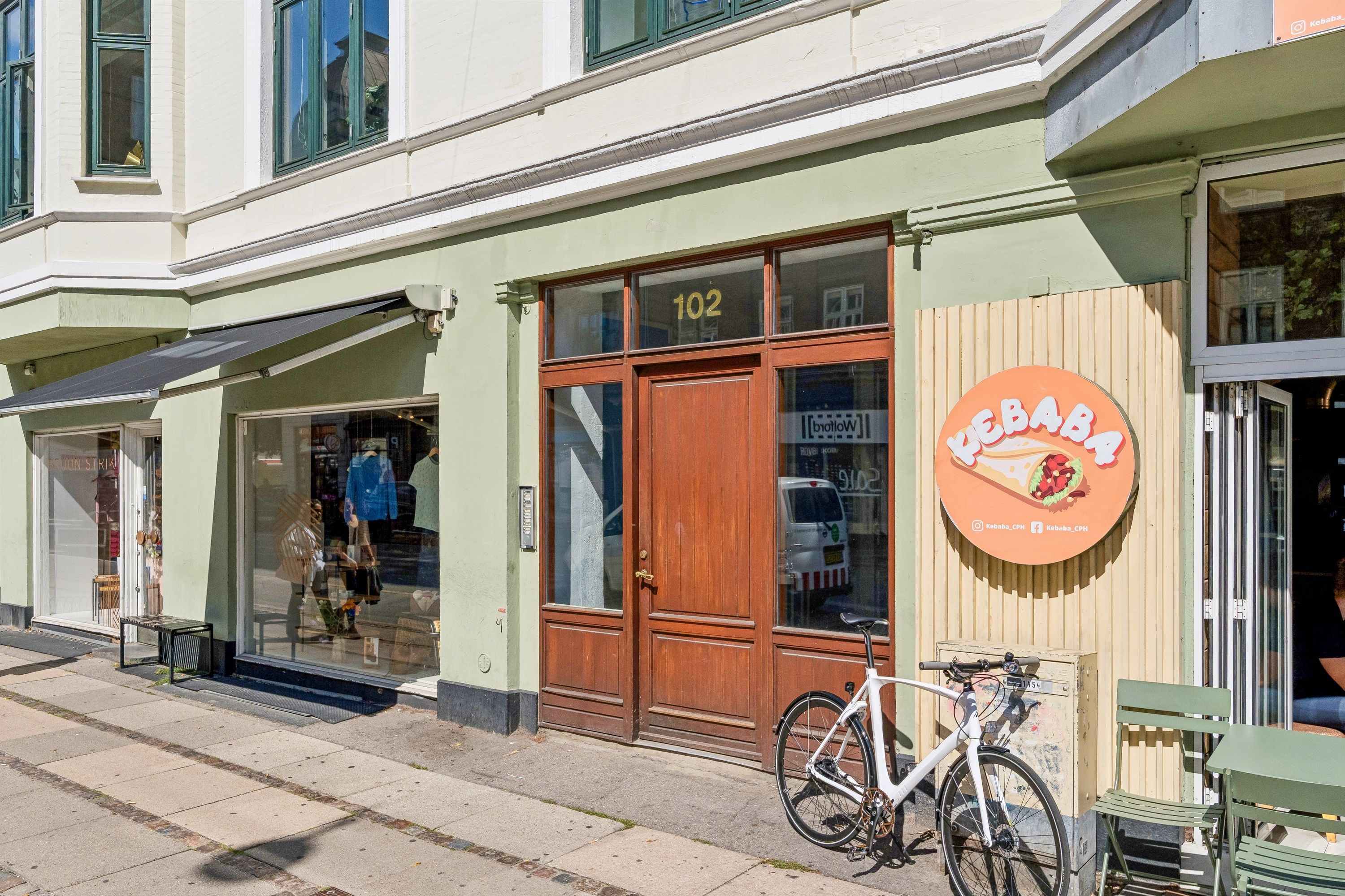En sømløs grøn facade med et vindue og en åben øvre terrasse med møbler og en hvid cykel i forgrunden.
