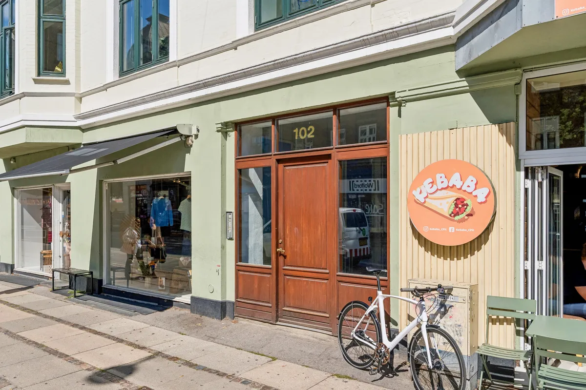 En sømløs grøn facade med et vindue og en åben øvre terrasse med møbler og en hvid cykel i forgrunden.