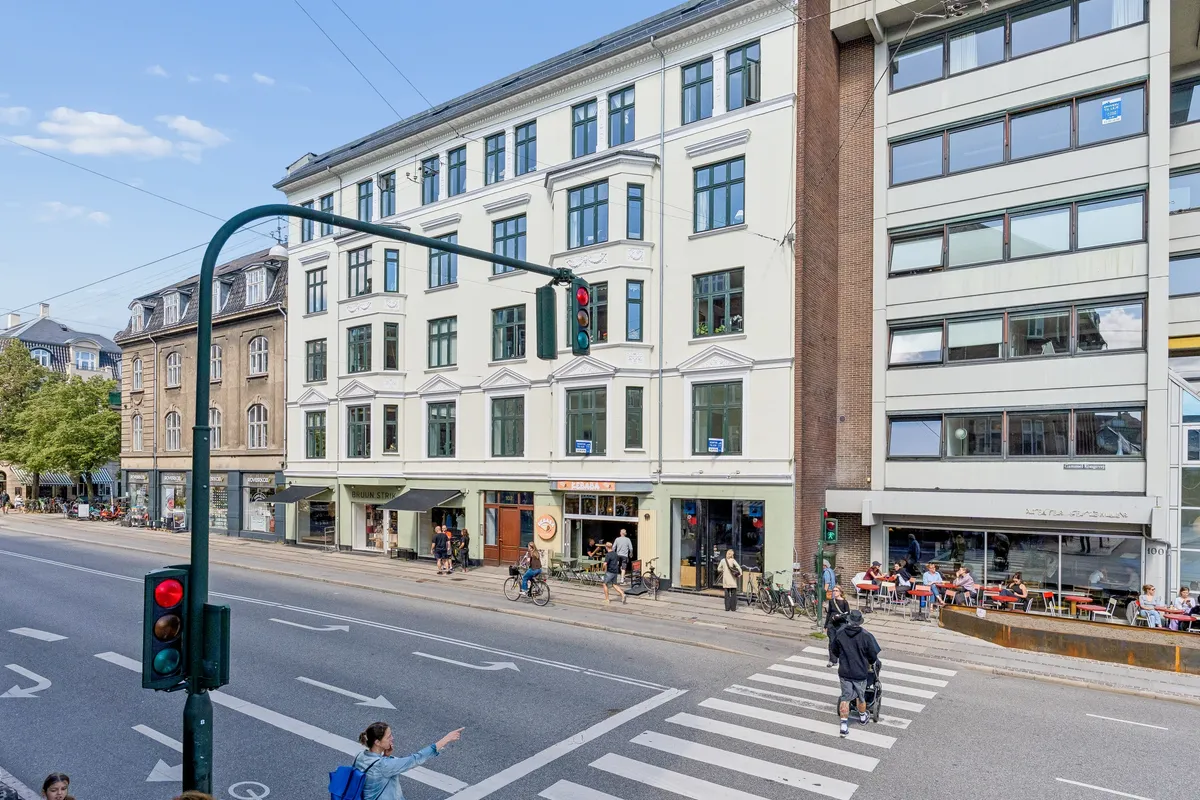 Gammel Kongevej med store bygninger, gågade, cykler, folk og trafiklys på en solrig dag