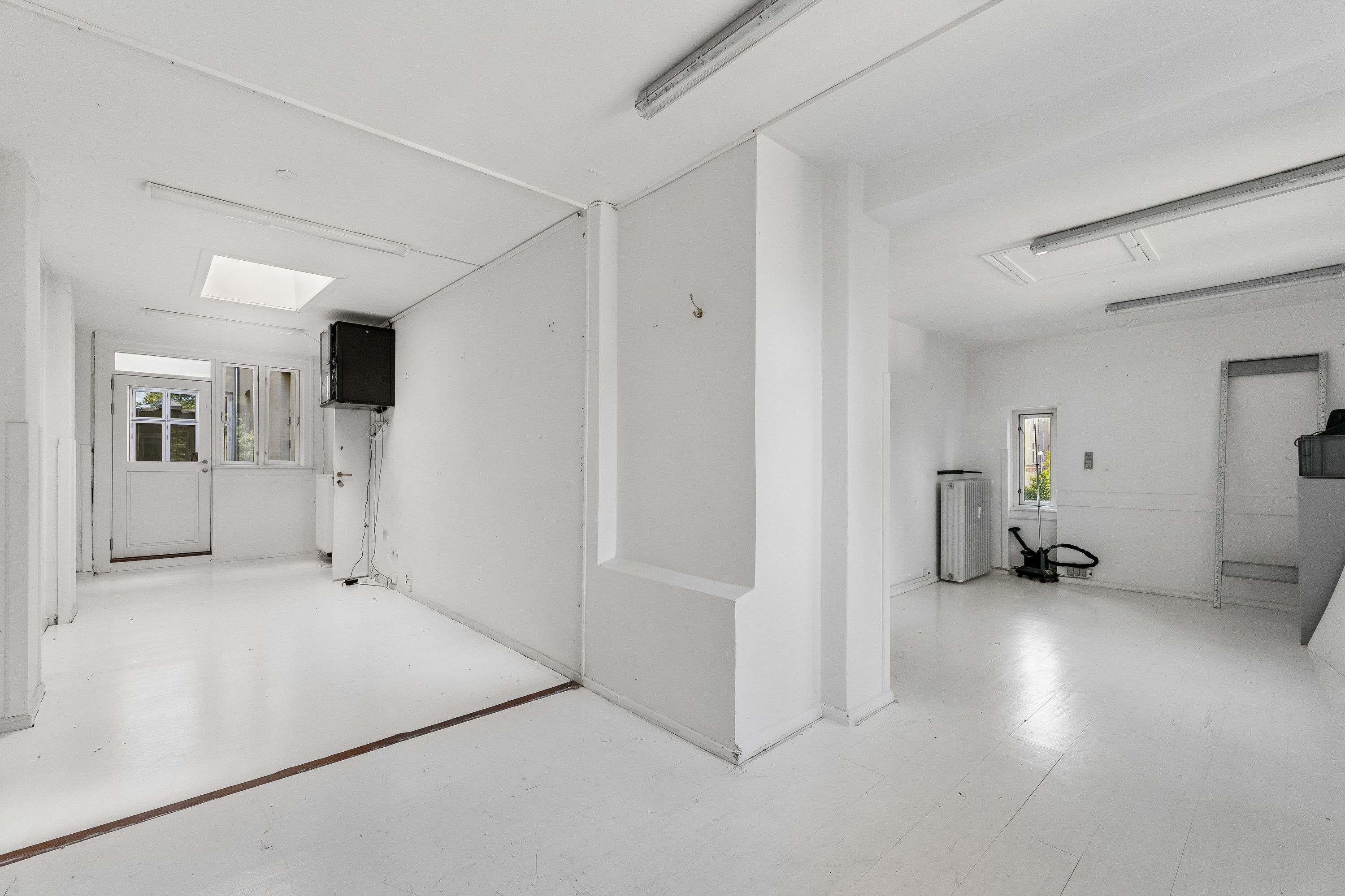 Kontor til leje med en stor, ren og lyset rummelighed, hvor der er et hvidt loft og hvide vægge. Der er en åben dør og et vindue samt en apparat og en hængekrog
