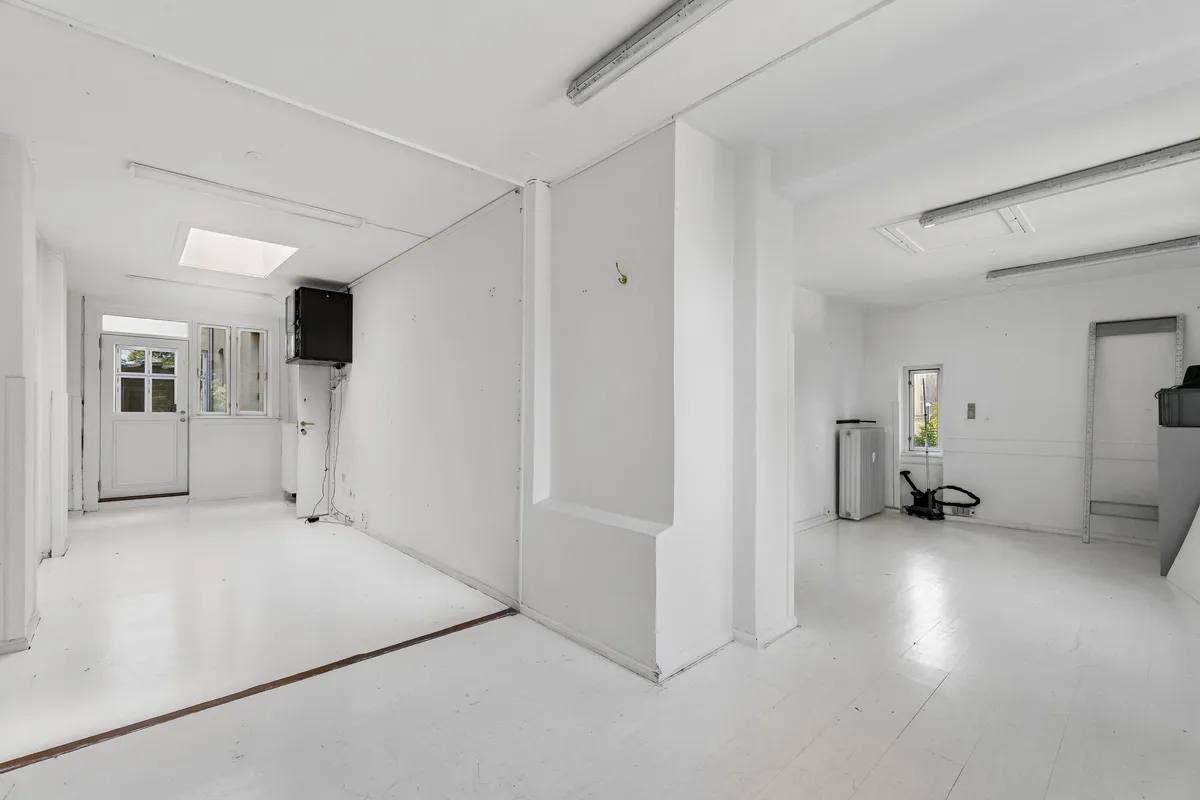 Kontor til leje med en stor, ren og lyset rummelighed, hvor der er et hvidt loft og hvide vægge. Der er en åben dør og et vindue samt en apparat og en hængekrog