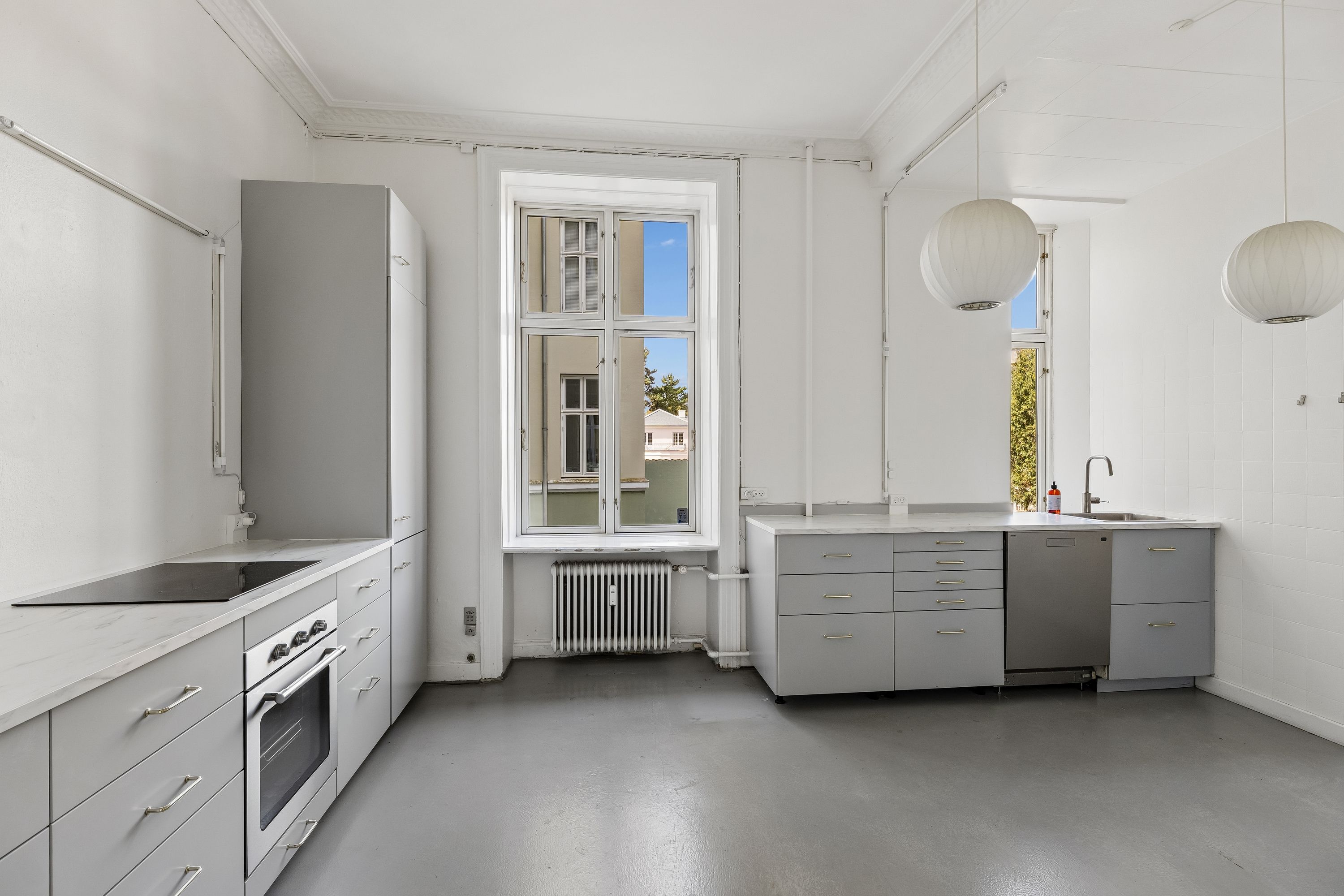Kontor med moderne og funktionel indretning, hvid væg, lyse loftslamper, stort vindue og en radiator og ovn