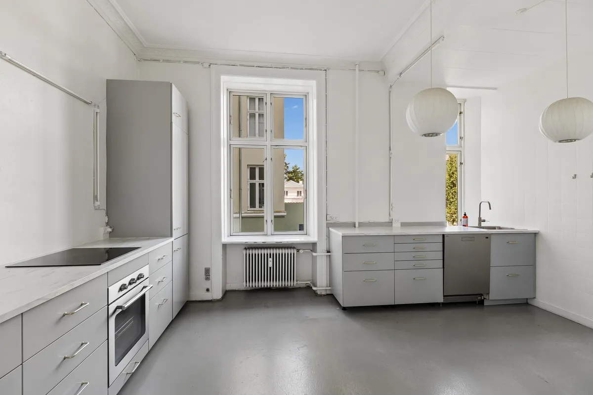 Kontor med moderne og funktionel indretning, hvid væg, lyse loftslamper, stort vindue og en radiator og ovn