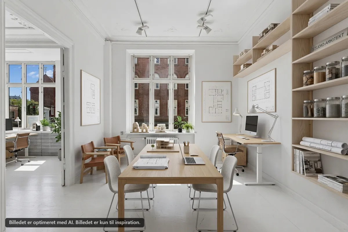 Nydelig og moderne møbleret kontor med store vinduer og masser af lys. I loftet hænger flere lysekroner. Der er flere skriveborde med moderne stole og en stor mødesal med langt borde og stole.