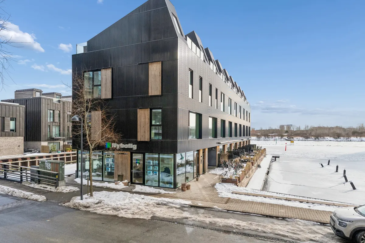 Moderne og luksuriøs erhvervslejemål på Teglholmens Østkaj 50 med udsigt over isdækket vand. Bygningen er udstyret med glasvinduer og træskodder.