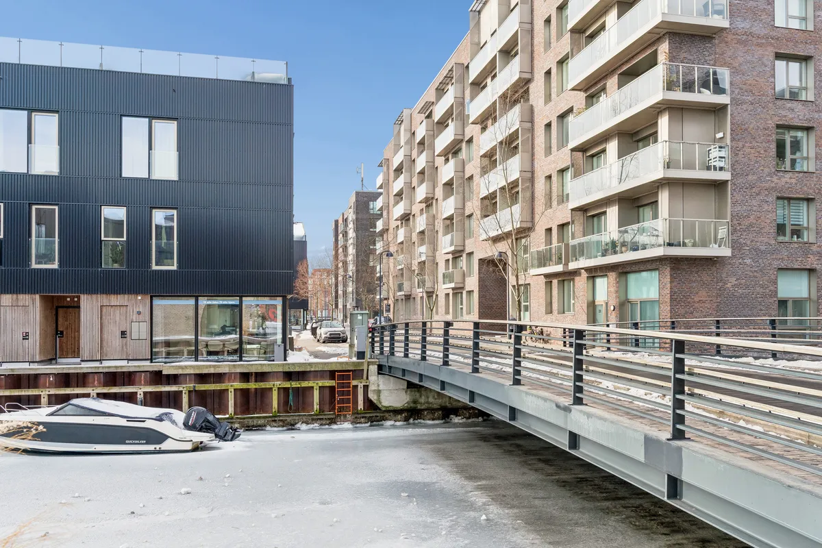 Lejlighedsbygning med glasfacade og balkoner og en båd parkeret ved kajen og en bro foran