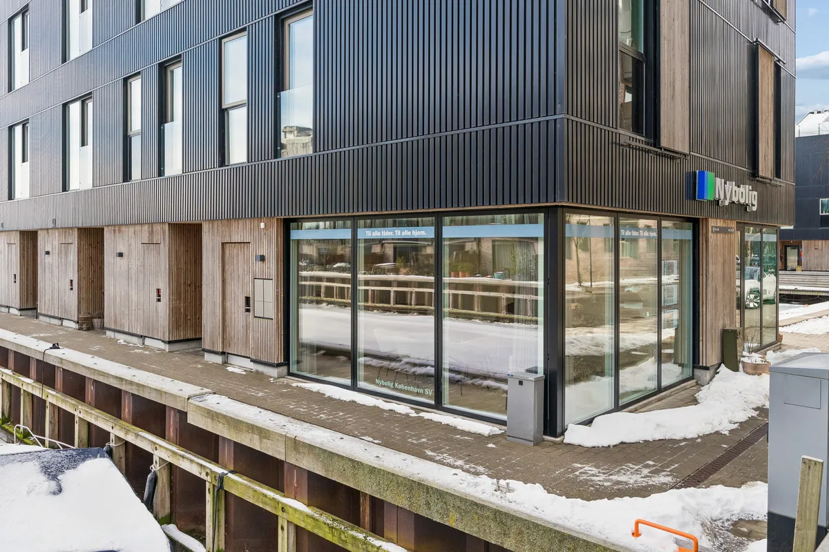 Moderne bygning med sort facade og store glasruder med Nybølle logoet og teksten "Til alle tider. Til alle hjem"
