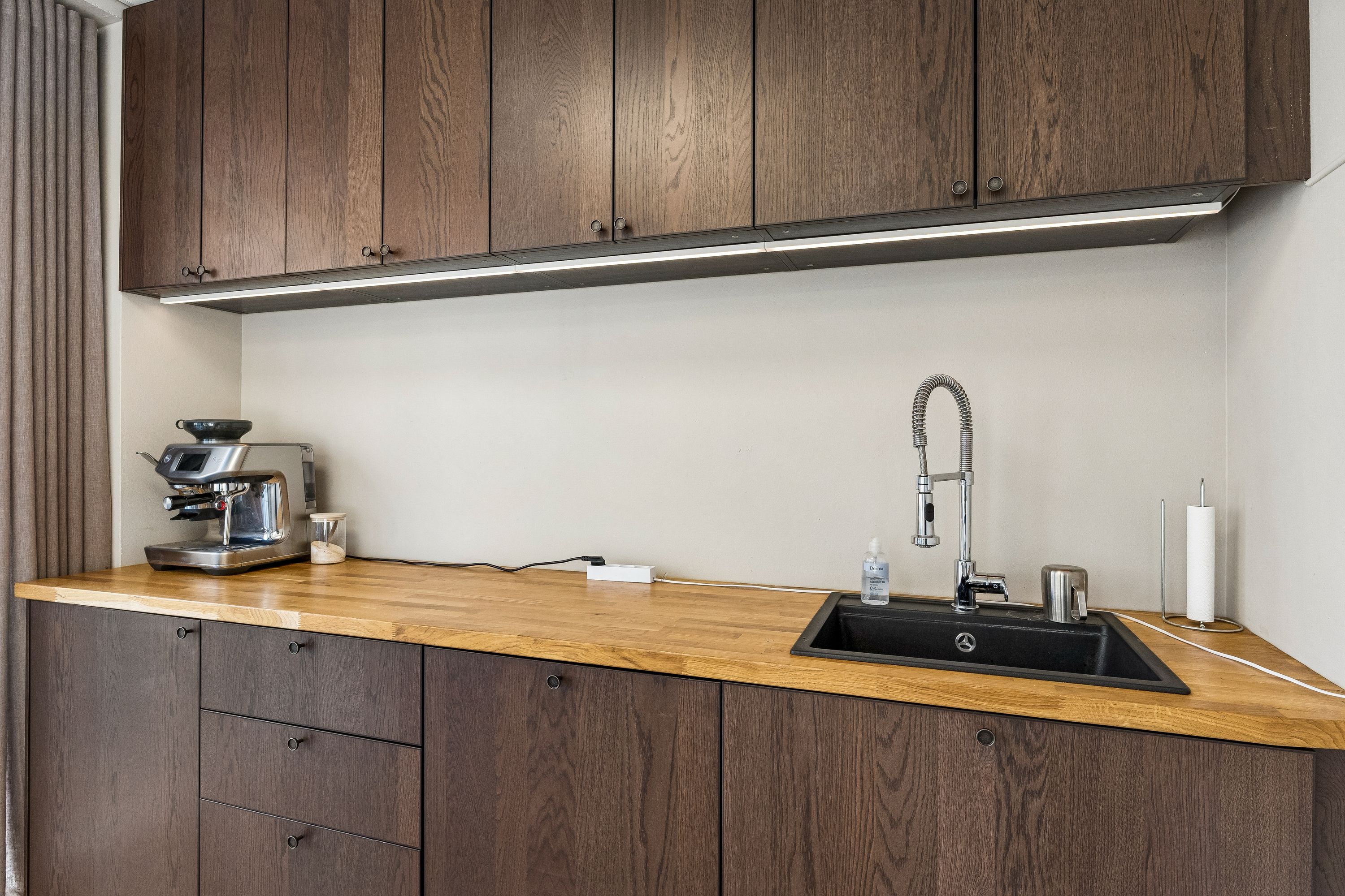 Lyse trækøkken med kaffemaskine og vandhaner. Sorte skraldespande og lyse træskuffer. Komplet med underskabe, højskabe og hvidt skarpt gulv.