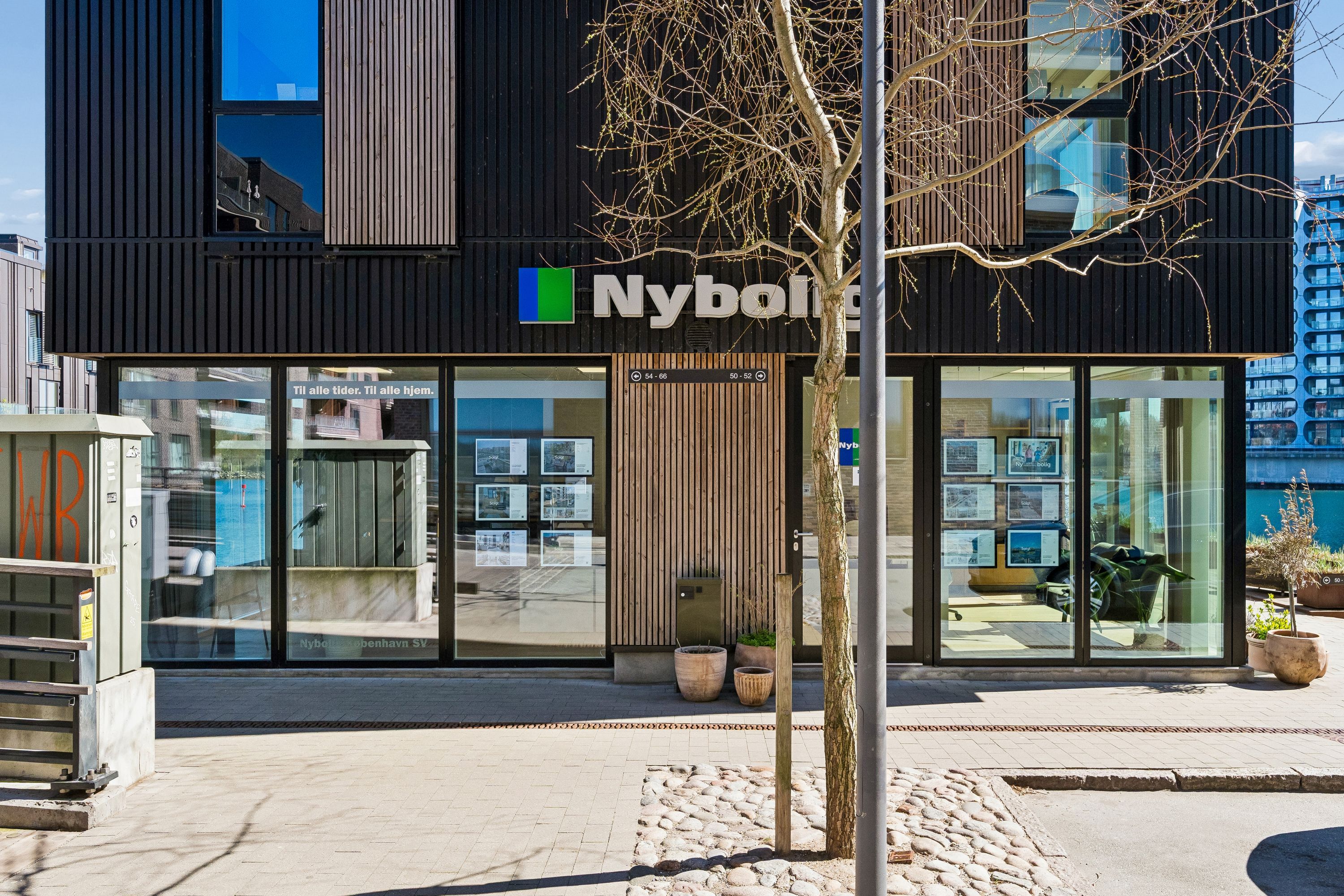 Butik til leje på Teglholmens Østkaj 50 i København SV med moderne facade og store glasvinduer, indrettet med tre store potteplanter og reklamefotos inde