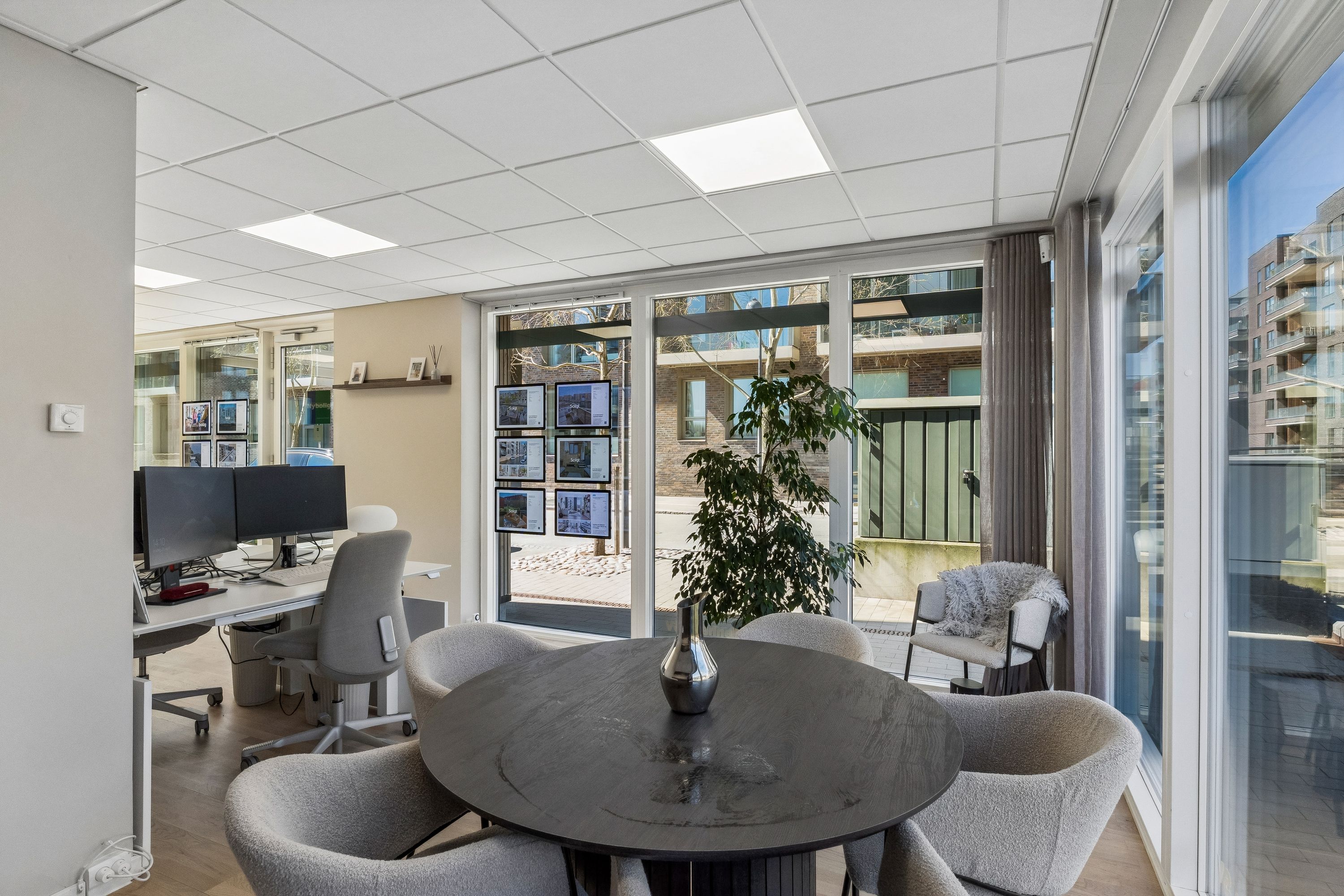 Kontor med bord, stole og computere, indretning med planter, glasvinduer og vægmontrerede fotos