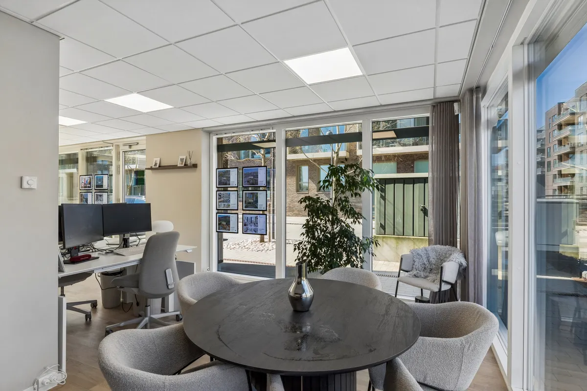 Kontor med bord, stole og computere, indretning med planter, glasvinduer og vægmontrerede fotos